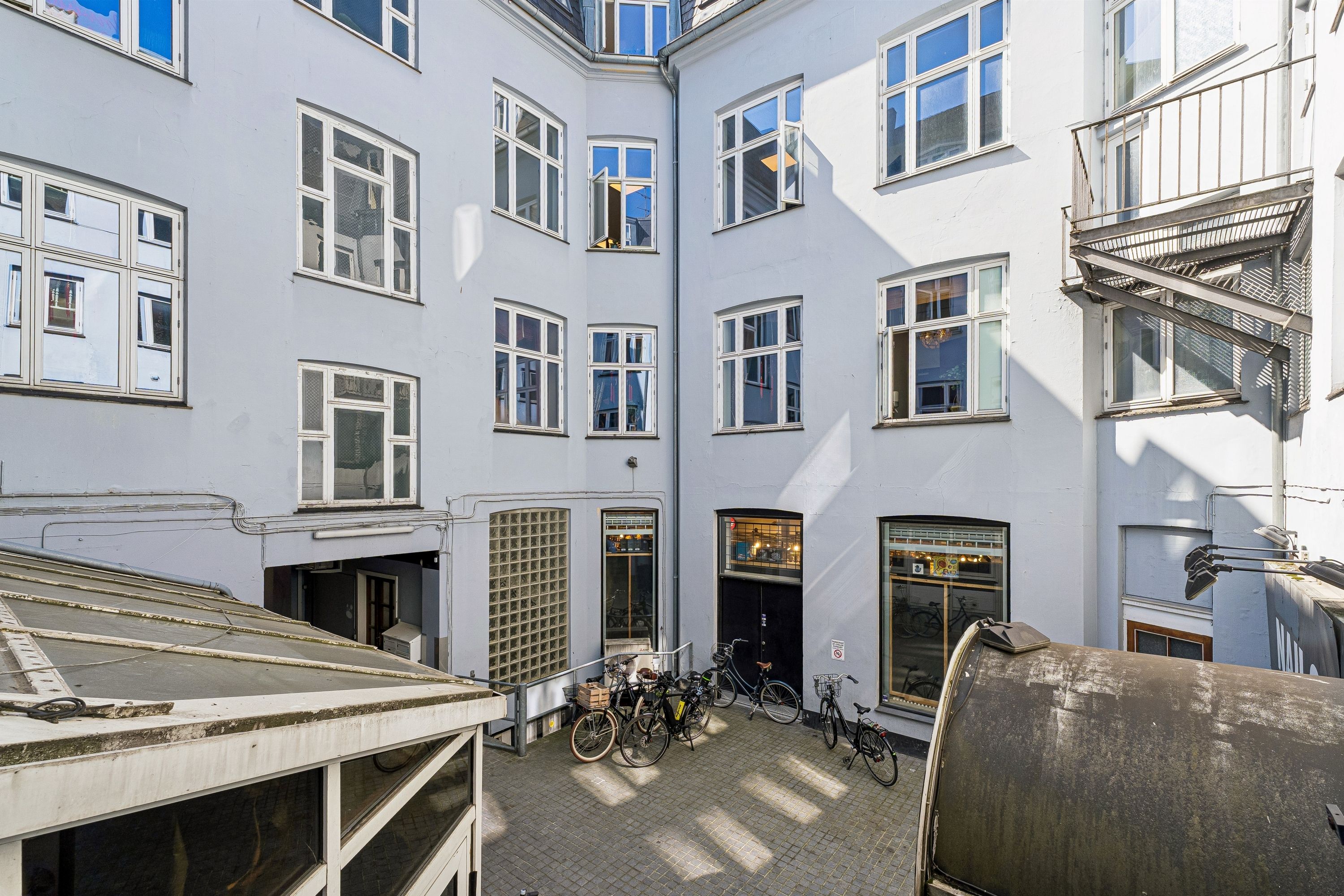 Kontor med mange vinduer og højloft i City. 5 cykler parkeret foran døren. 2 glasdøre til kontor og en lille skur til cyklerne.