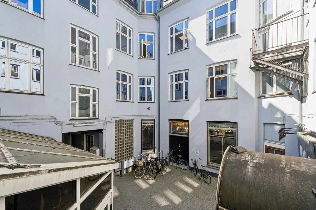 Kontor med mange vinduer og højloft i City. 5 cykler parkeret foran døren. 2 glasdøre til kontor og en lille skur til cyklerne.
