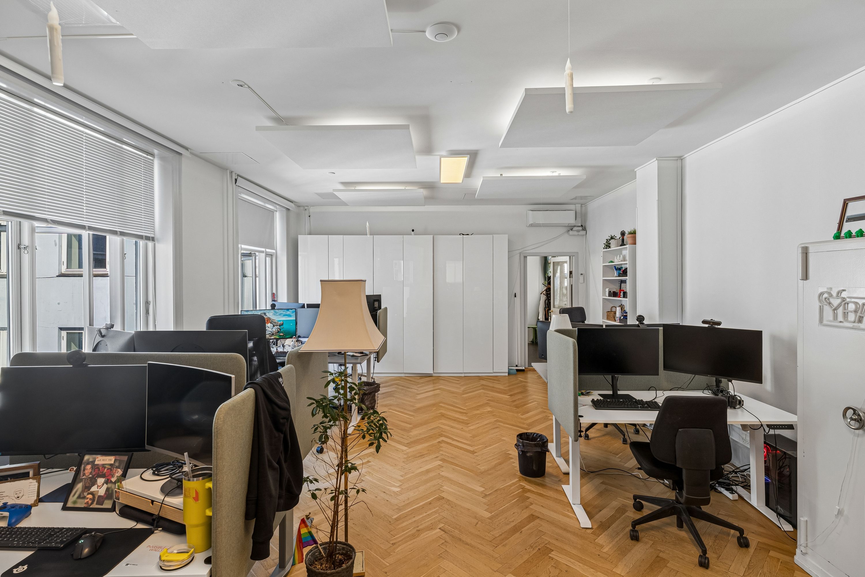 Moderne kontor med højloft, lysevinduer, skriveborde, computere, stole, gulv og plante i en minimalistisk indretning med hvide vægge og trægulv