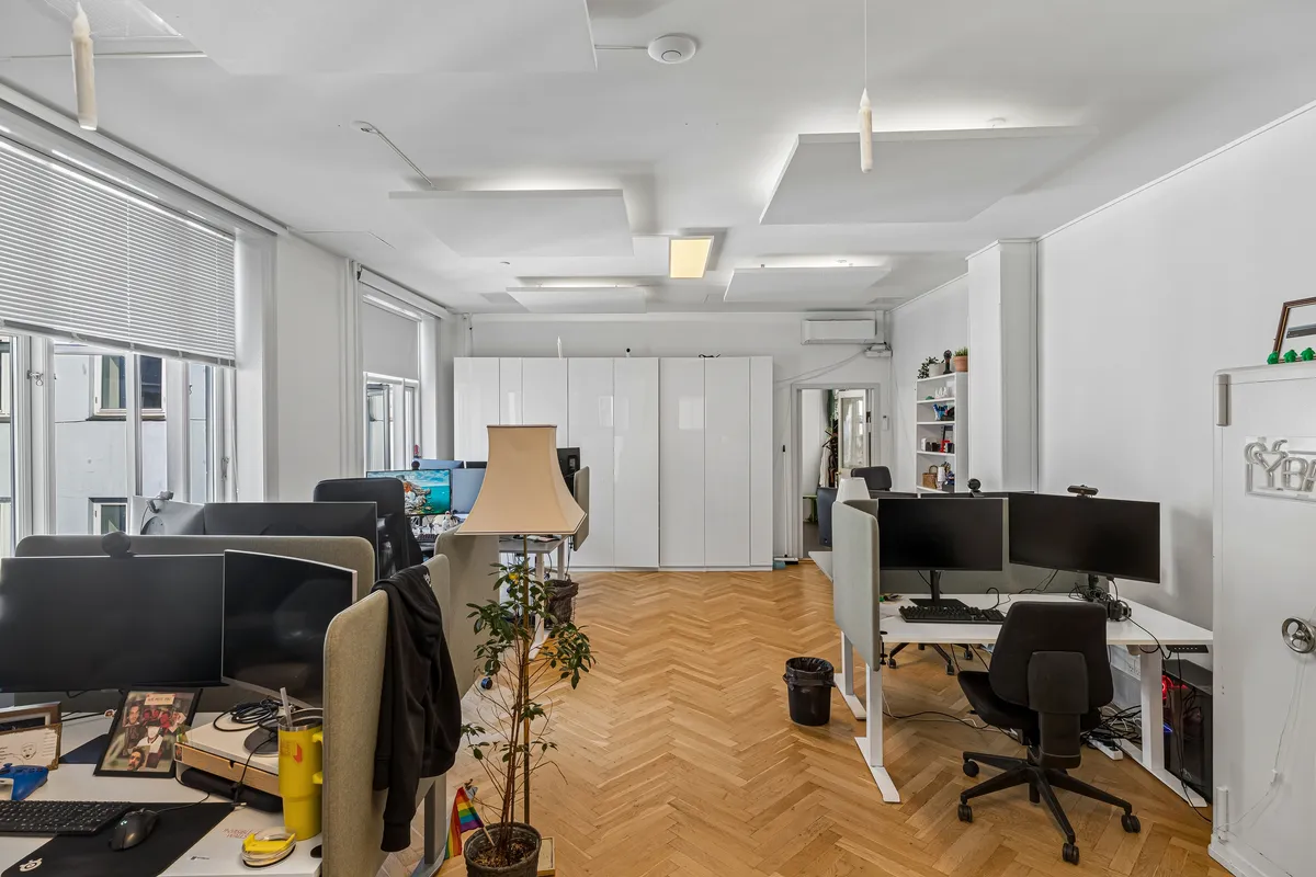 Moderne kontor med højloft, lysevinduer, skriveborde, computere, stole, gulv og plante i en minimalistisk indretning med hvide vægge og trægulv