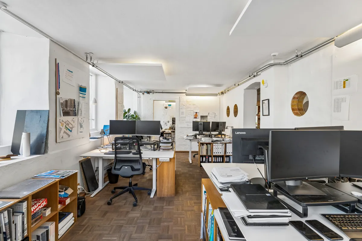 Kontor med lyse lofter, gulve og hvide vægge med lysekroner og møbler inklusiv skriveborde, stol, computer og bibliotek.