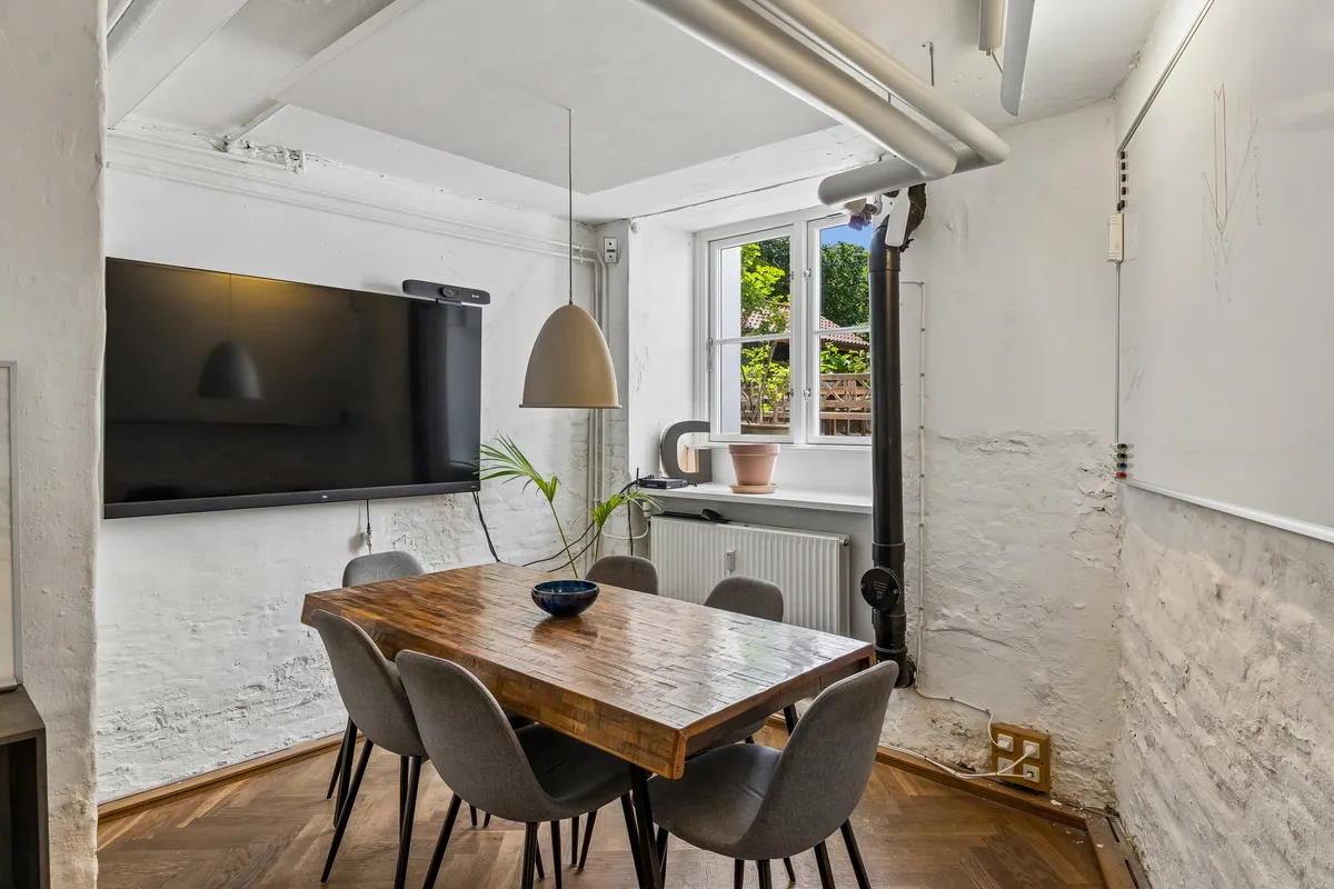 Kontor med moderne møbler, bord og stole, plante og tv på væggen, radiator og vinduer med udsigt til haven