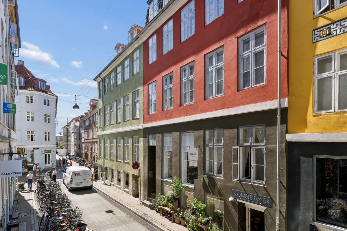 En lille gade i København med flere bygninger og gadeblik. En hvid lastbil kører ned ad gaden. Der er flere cykler parkeret ved siden af gaden.