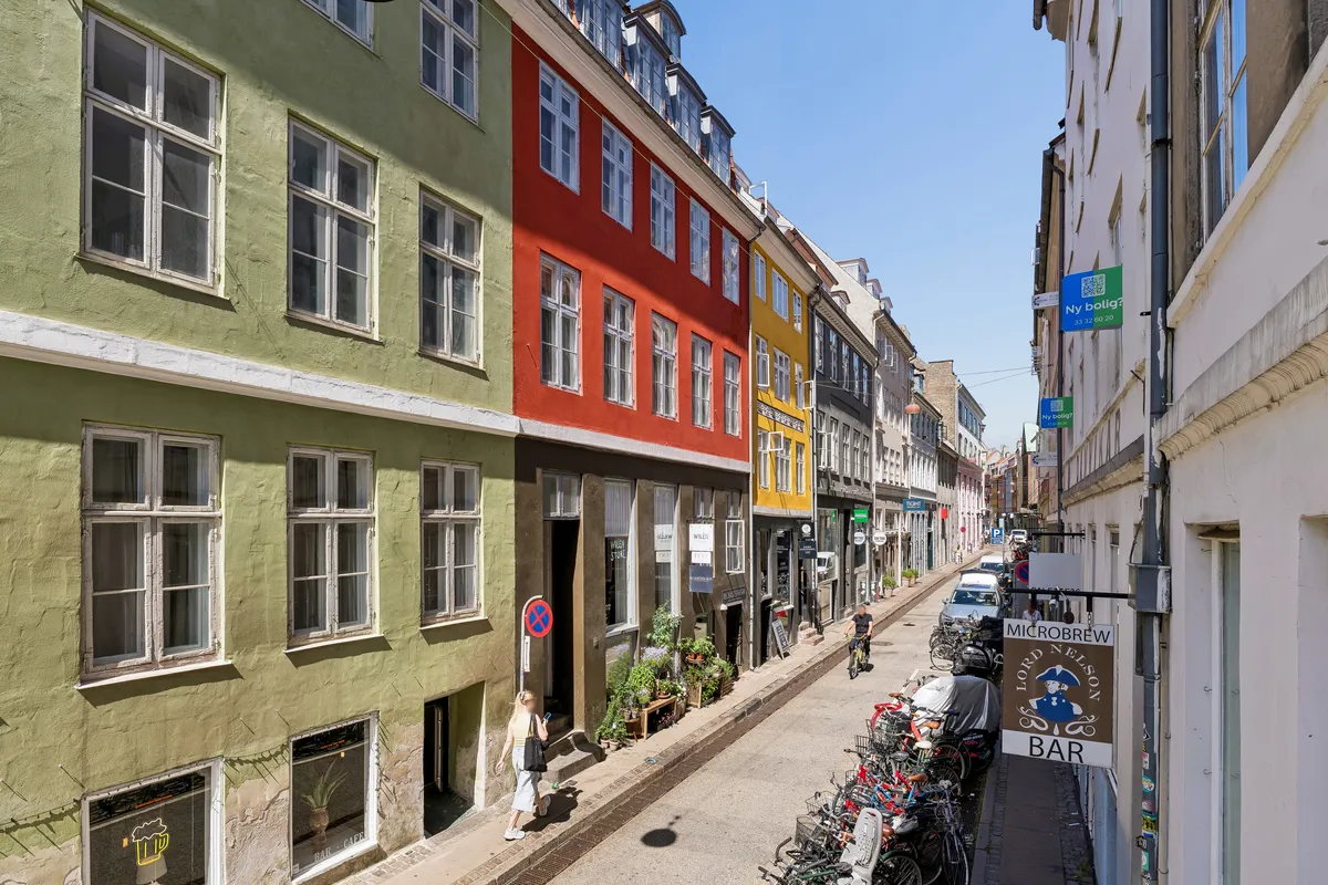 Mennesker går langs en gågade med forretninger, hvor der står skilt for Microbrew Bar, og der er mange cykler parkeret på siden af gaden