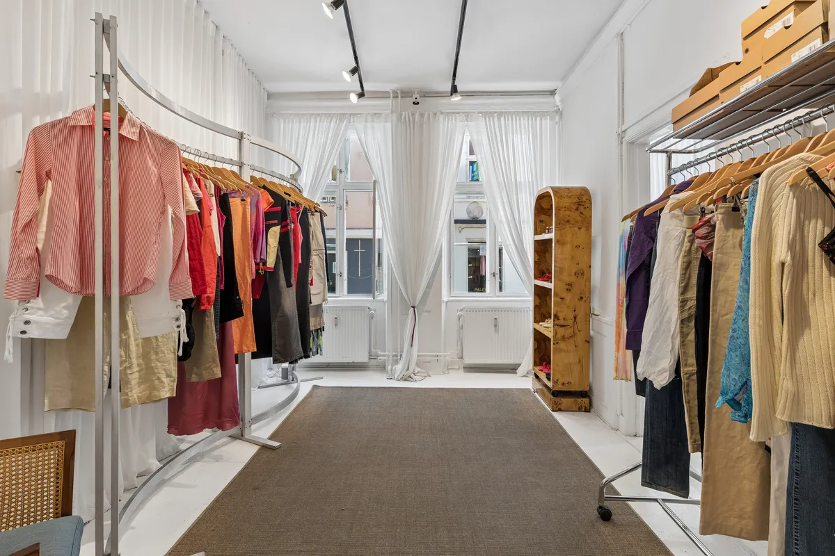 Lys og rummelig butik med klædeskab, hængeklæder, hvidt gulv og lysegardiner. Lyse og farverige tøjstørrelser og -typer. Moderne indretning med lyse og rene vægge