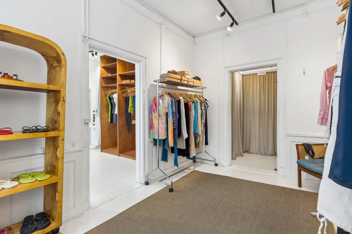 Butik med hængehylder, tøjstative og åbne garderobeskabe. Gulvet er dækket med tæppe og træhylde. Lyskryds og lysekroner på loftet.