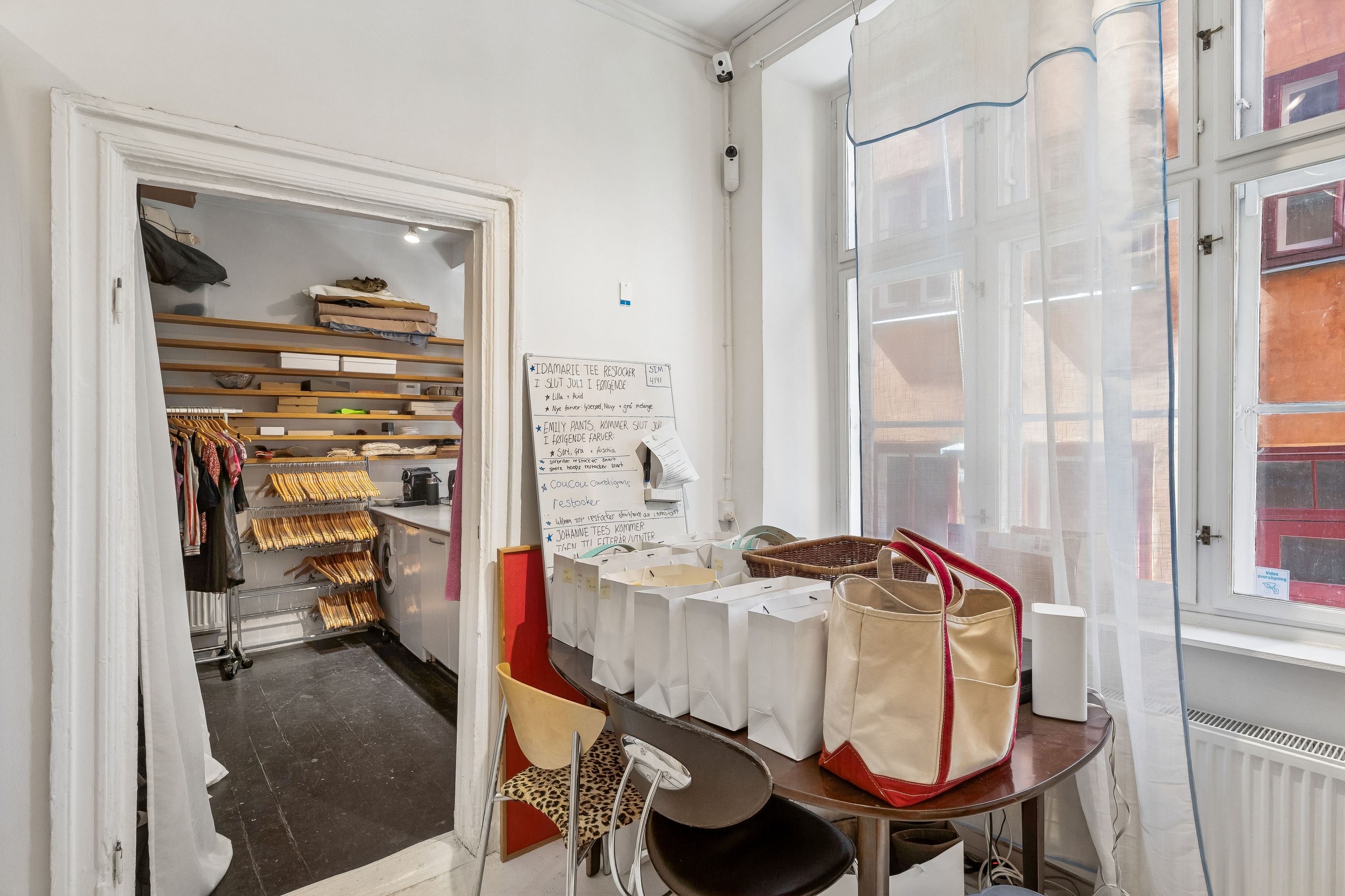 Københavns historiske bykerne med en charmerende og lyse butik på 71 m² til leje med indvendige hængehylder, hvidt pap og et højt skrivebord med noter og toppesko.