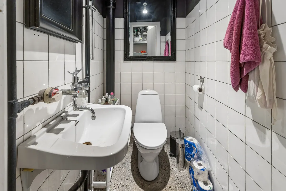 Billet for leje butik i København med toilet, håndvask og tøjvask. Bag toilettet er en række toiletpapir, og en pink håndklæde er hængende på væggen.
