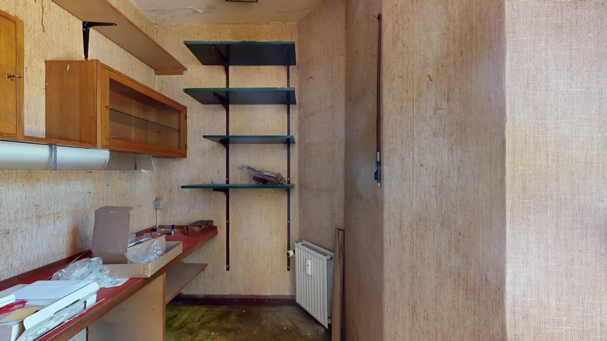 Et lille og ubenyttet lagerrum med tre slanke hylder og en hvid radiator samt flere kasser og emballage.