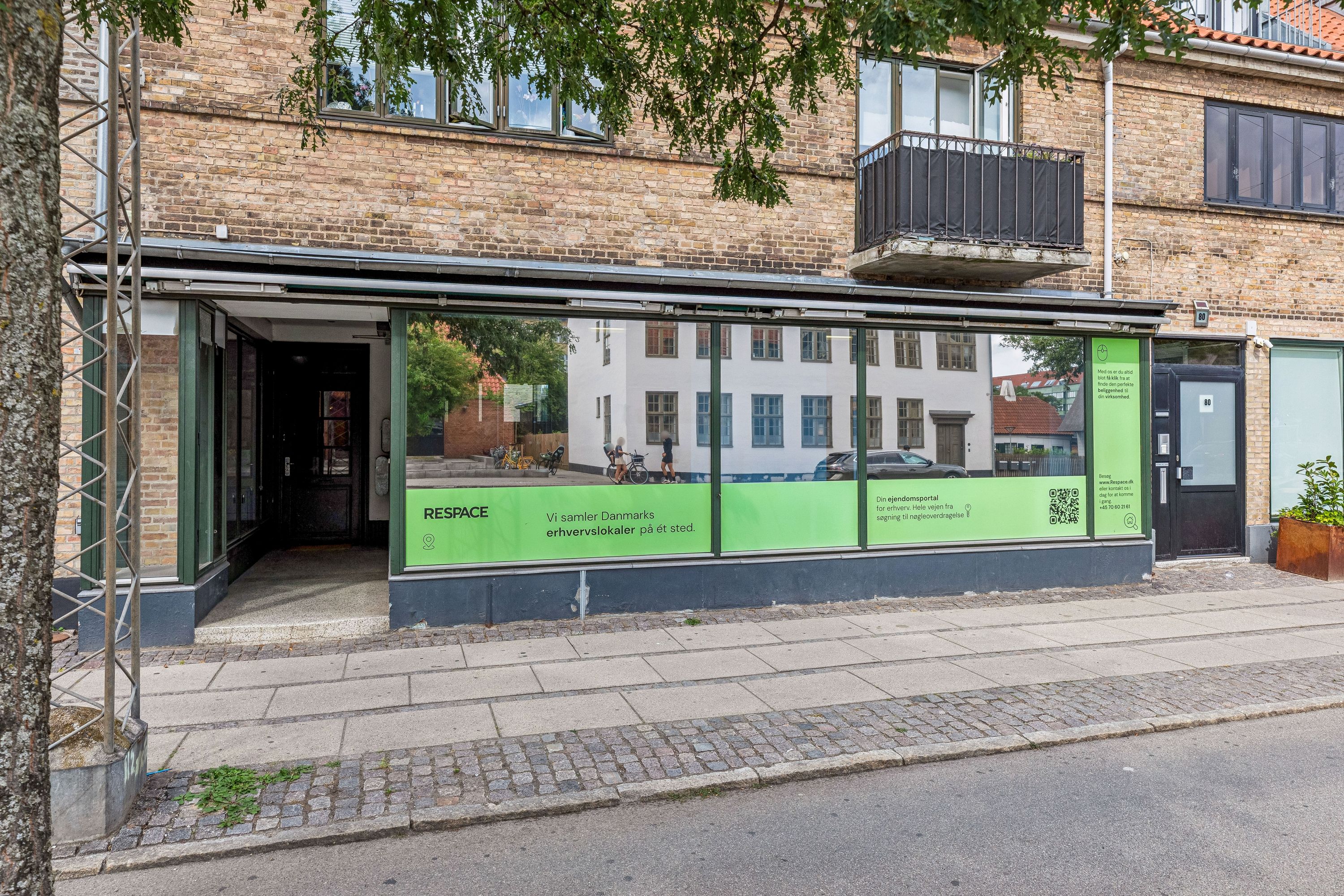 Kontor til leje på Godthåbsvej 82, Frederiksberg. Bygningen har store glasruder og står ved siden af slagterbutikker og sportsforretning. Der er en QR-kode på facaden.