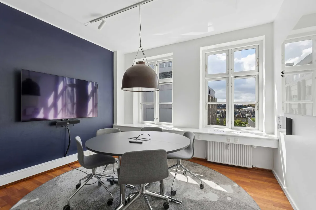 Rundt mødelokale med tv og skrivebordslampe i lyst kontor med eksklusive faciliteter og store vinduer i lysegrå og hvid farve