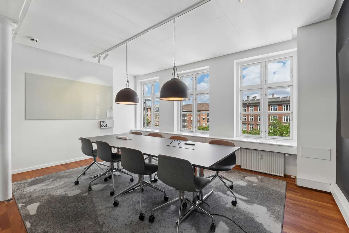 Kontor med moderne møbler, høj loftshøjde og lyse vinduer, som giver en åben og inspirerende arbejdsplads i et dynamisk kontorhus på Vesterbro.
