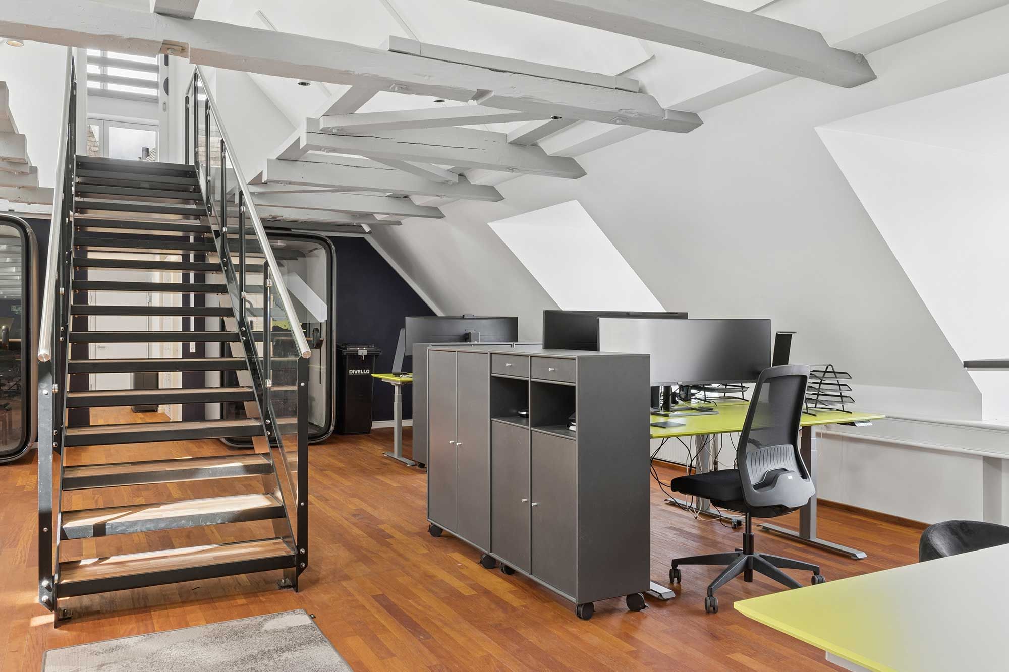 Indvendigt kontor med højloft, moderne møbler, lysegul gulvbelægning og glastrapper for nem adgang til loftsrummet. Kontoret har eksklusive faciliteter og udstråler en dynamik.