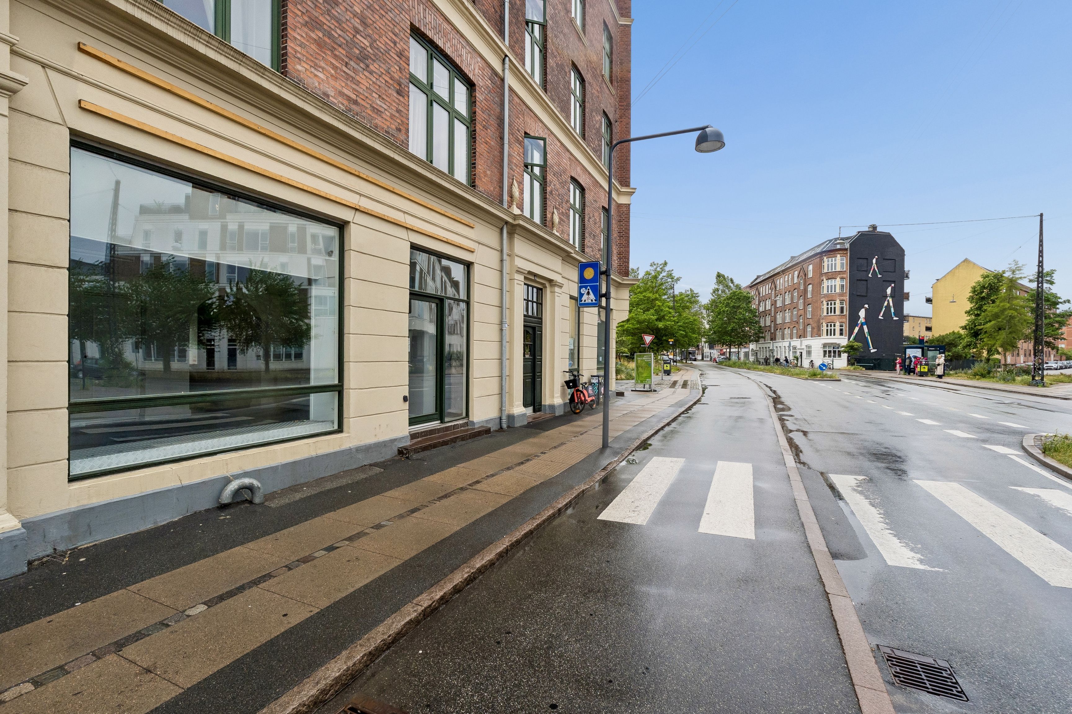Erhvervslejemål med store udstillingsvinduer og cykelparkering på gågade med mærkbare stier og grønne områder bagved
