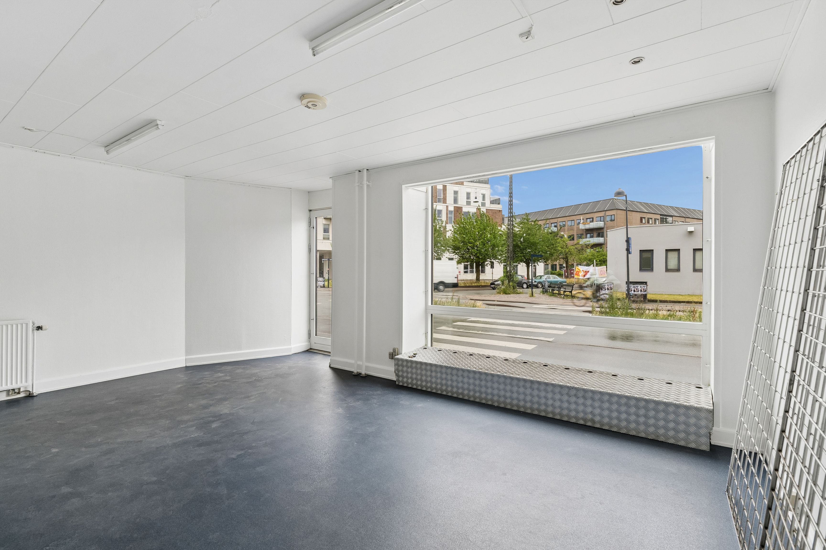 Store lejemål med store glasvinduer og lyse lofter. Møbelfri og rentabel lejebolig med grønne træer og gadeblik på gården