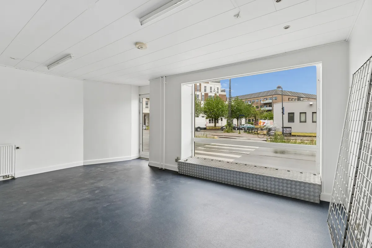 Store lejemål med store glasvinduer og lyse lofter. Møbelfri og rentabel lejebolig med grønne træer og gadeblik på gården