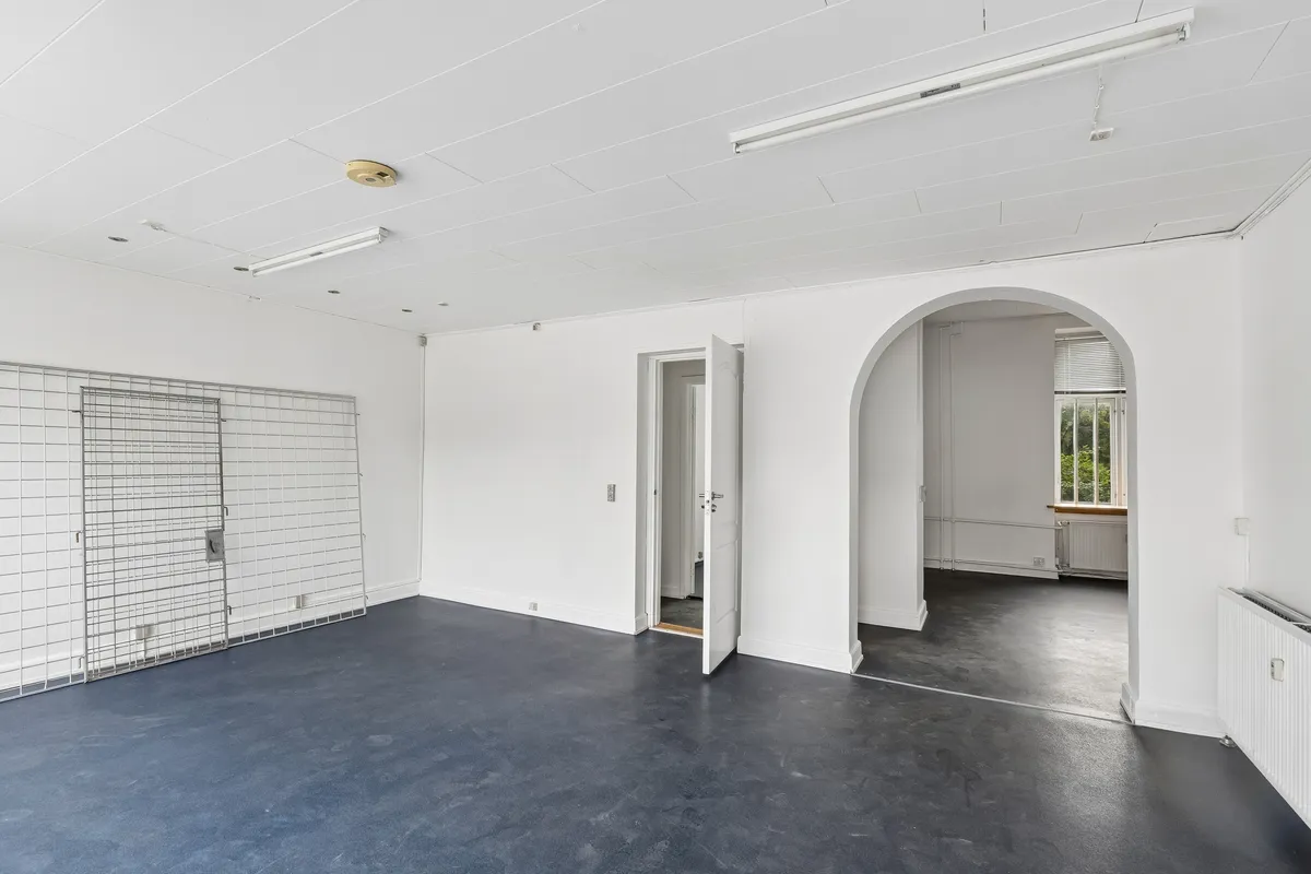 Lyst erhvervslejemål med store glasruder og åben dør og udstillingsvindue i en hvid malet lokal med højloft