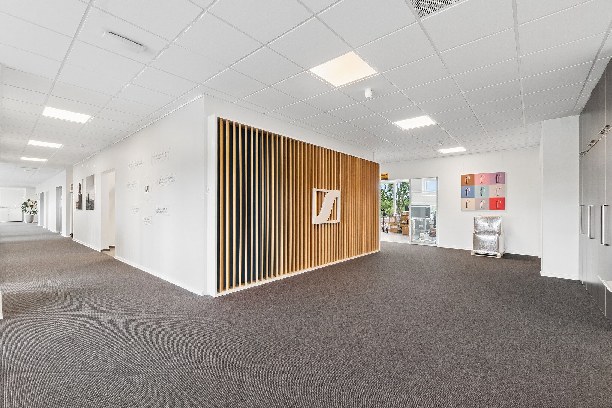 Kontorlejemål med flisegulv og hvidt loft. Moderne møbler og indretning. En væg med mønstret træ og Z-logo. Et stykke møbel og flere kasser på gulvet.