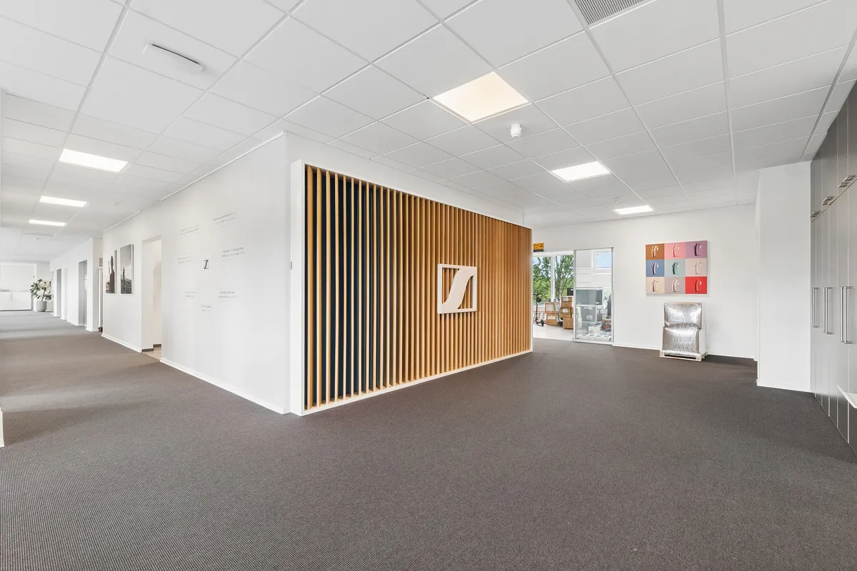 Kontorlejemål med flisegulv og hvidt loft. Moderne møbler og indretning. En væg med mønstret træ og Z-logo. Et stykke møbel og flere kasser på gulvet.