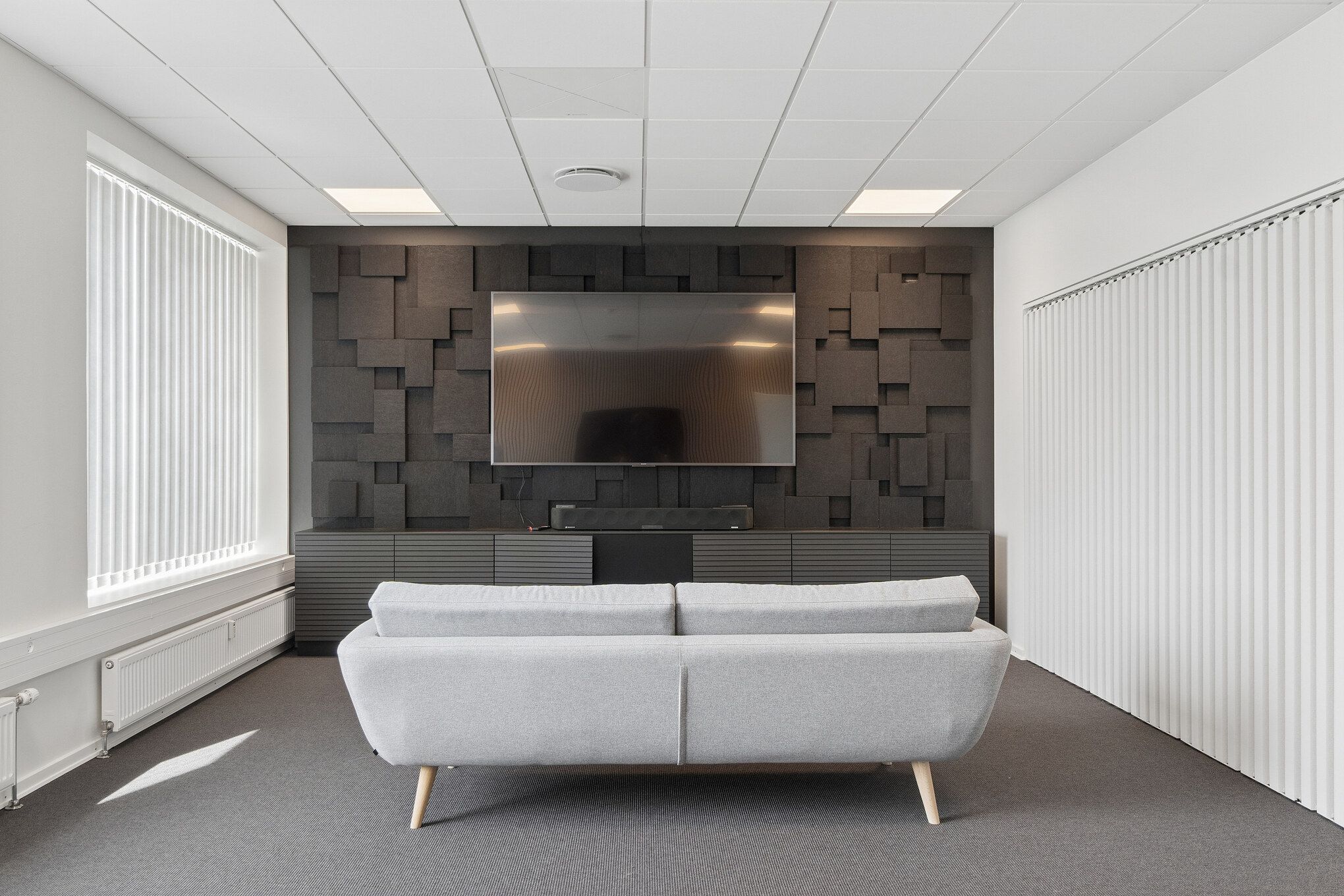 Kontor med sofa, stolpeventilatorer og tv. Kontor med lyse møbler og moderne design. Kontor med højt loft og hvide vægge.