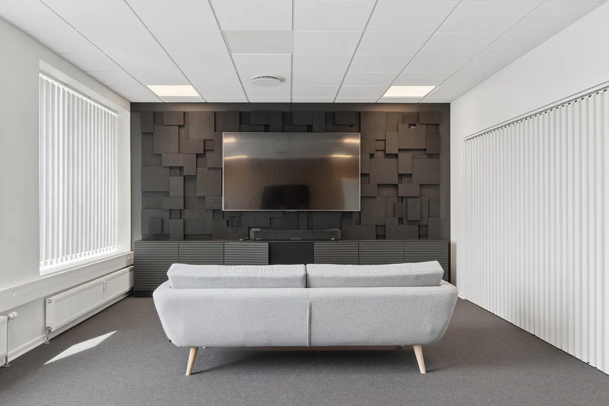 Kontor med sofa, stolpeventilatorer og tv. Kontor med lyse møbler og moderne design. Kontor med højt loft og hvide vægge.