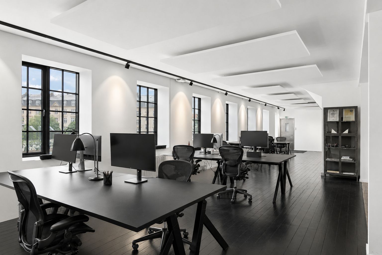 Kontorlokaler med lyse, indbydende rammer og moderne indretning, hvor skriveborde og stolpe udgør et ergonomisk arbejdsområde. Indbygget belysning og store vinduer skaber et produktivt og inspirerende arbejdsmiljø