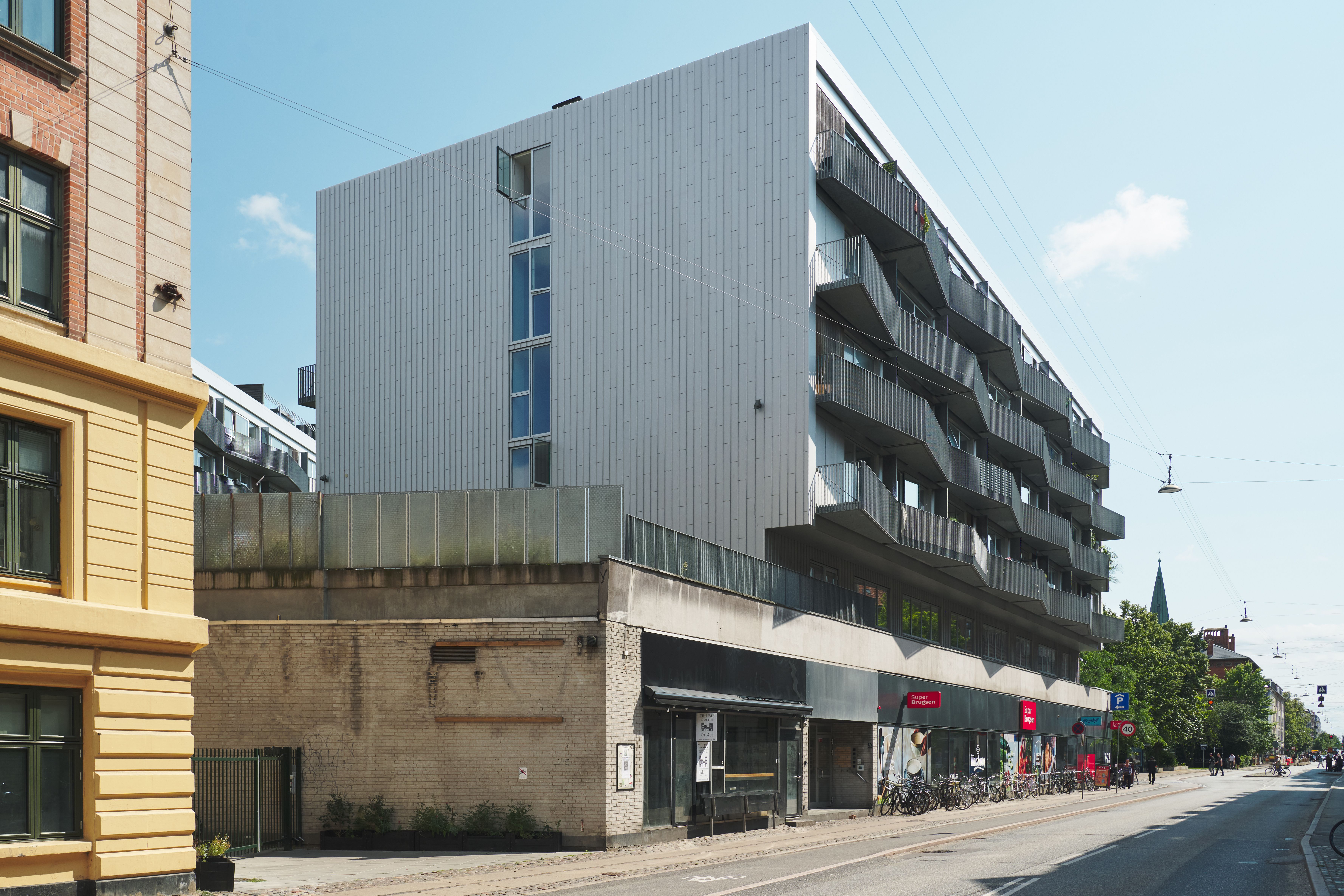 en stor højhusbygning med en hvid facade og terrasser, med en café i stueetagen og cykler udenfor