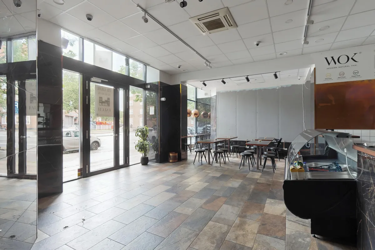 Inde i restauranten med moderne naturlige thailandske retter er der to store vinduer og et åbent gulv med krydsfinerbelagt træ. Der er to små borde med stole.