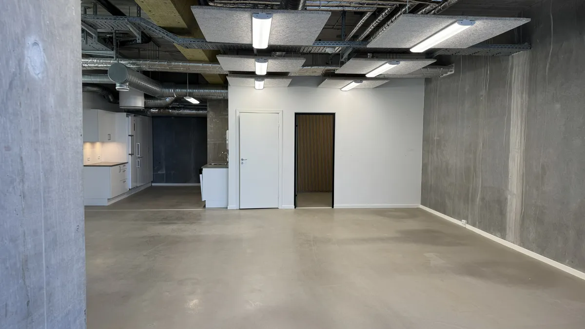 Ledig erhvervslejemål med 134 m² og lyse loftslamper, hvid trædør og grå væg, køkken med hvide skabe og lysegulv