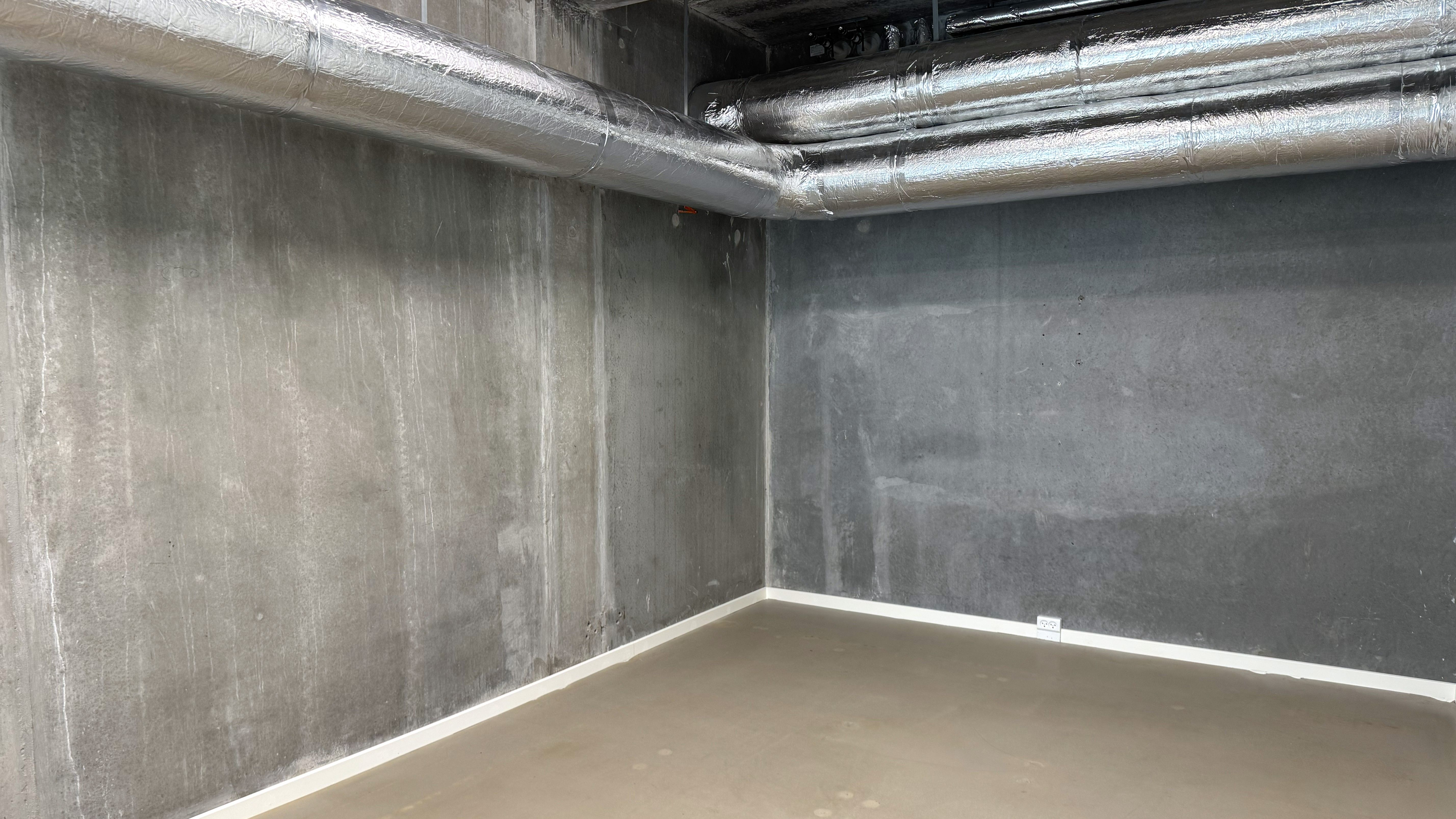 En rummelig kontorlokal i Frederikssund med betonvægge, hvide gulve og gulve. Væggene er belagt med aluminium og tekstil.