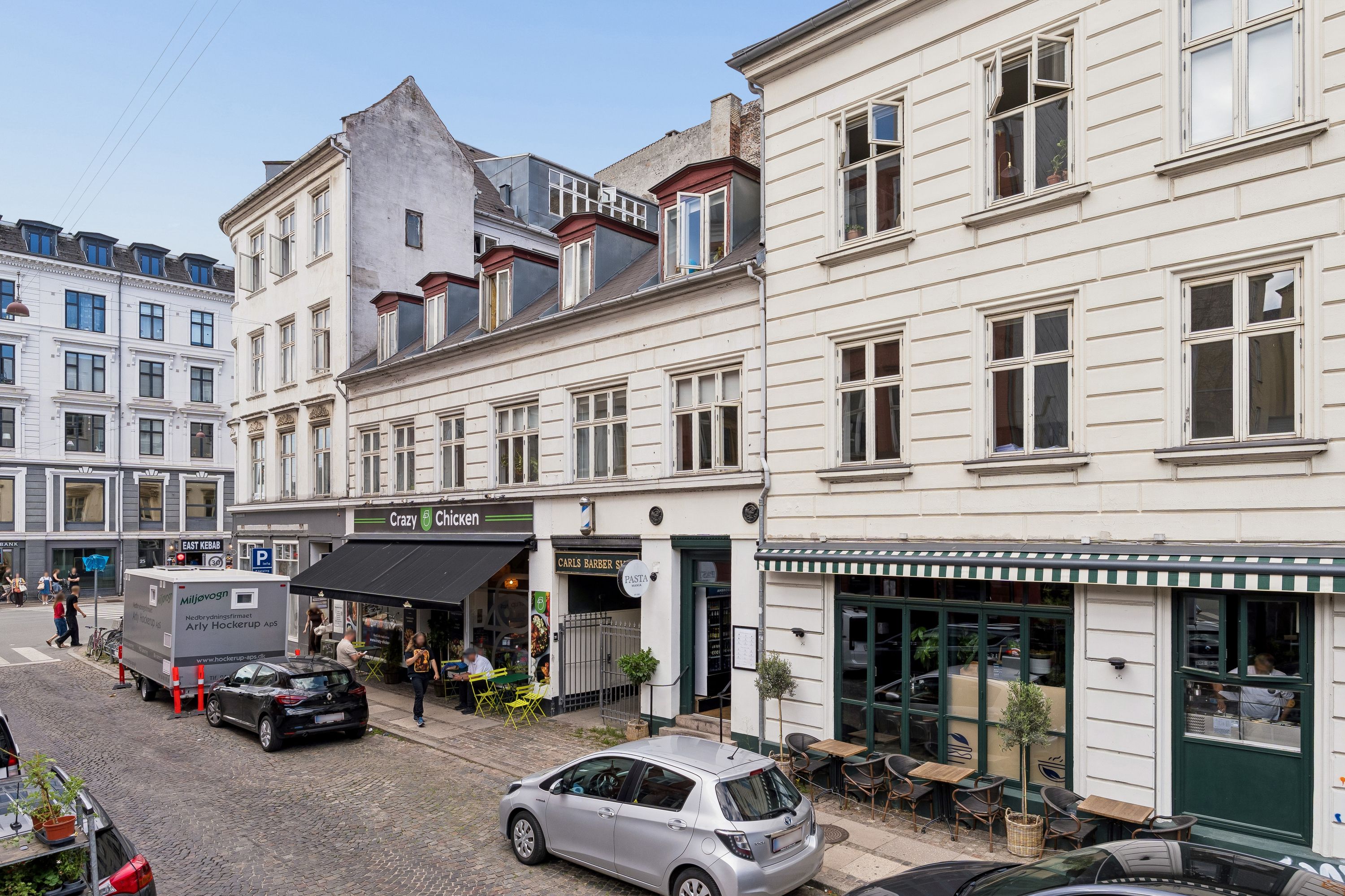 Kontor til leje på Rosenvængets Allé med flotte udsigtsvinduer og grønne plantager i forgrunden, og biler parkeret langs siderne af gaden
