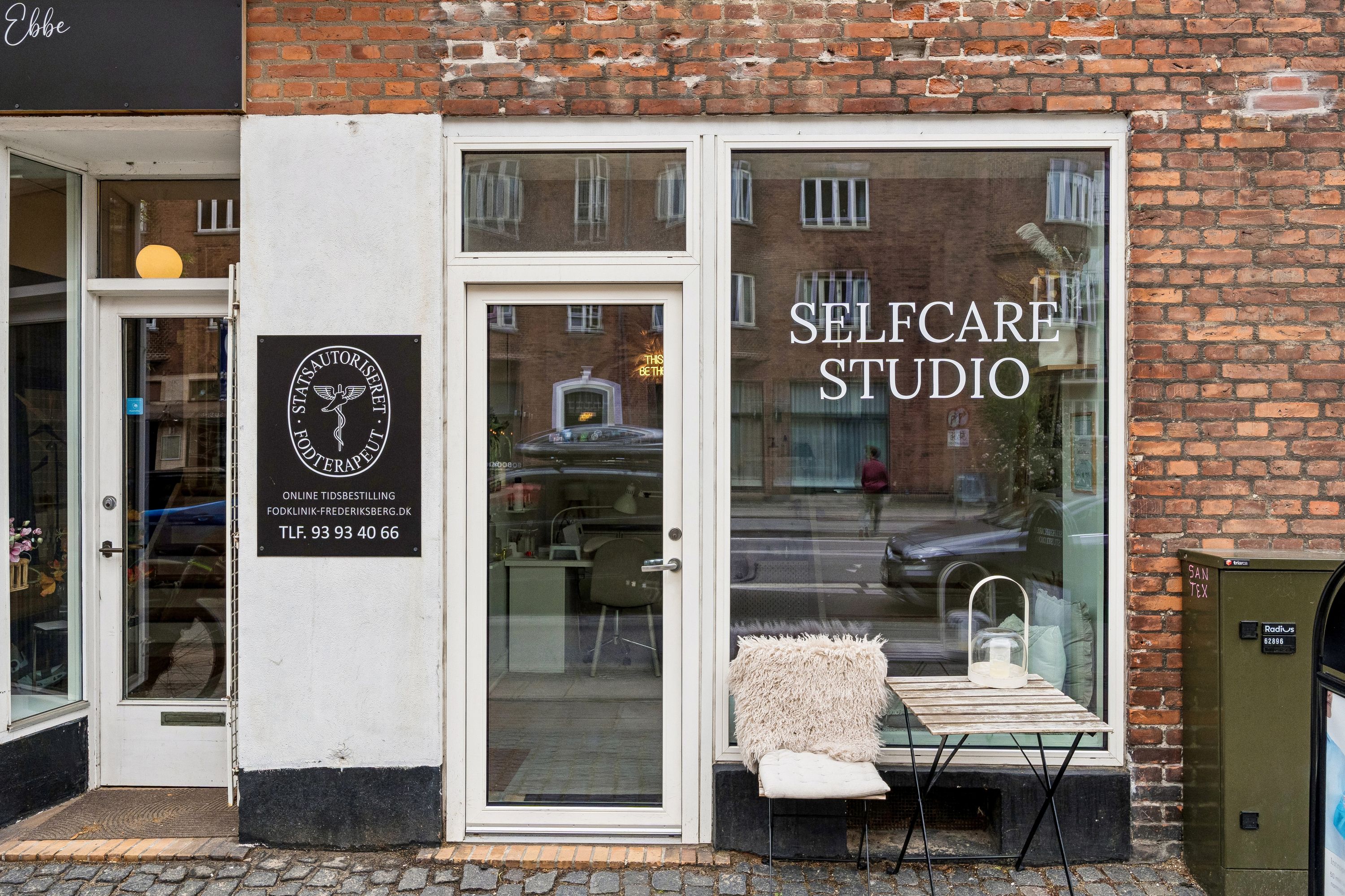 Butik med teksten Selfcare Studio på facaden, foran er der en lille hvid pude og et bord med en lampeskærm
