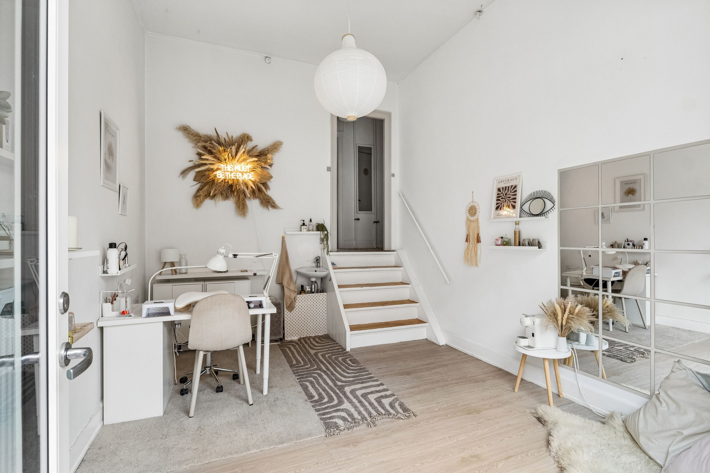 Lys og lyse interiør med hvidt loft, lysegrå gulv og hvide vægge. Et moderne kontor med skrivebord, stol, loftslampe og spejl. En stor spejlvæg og et sæt lyse tæpper.