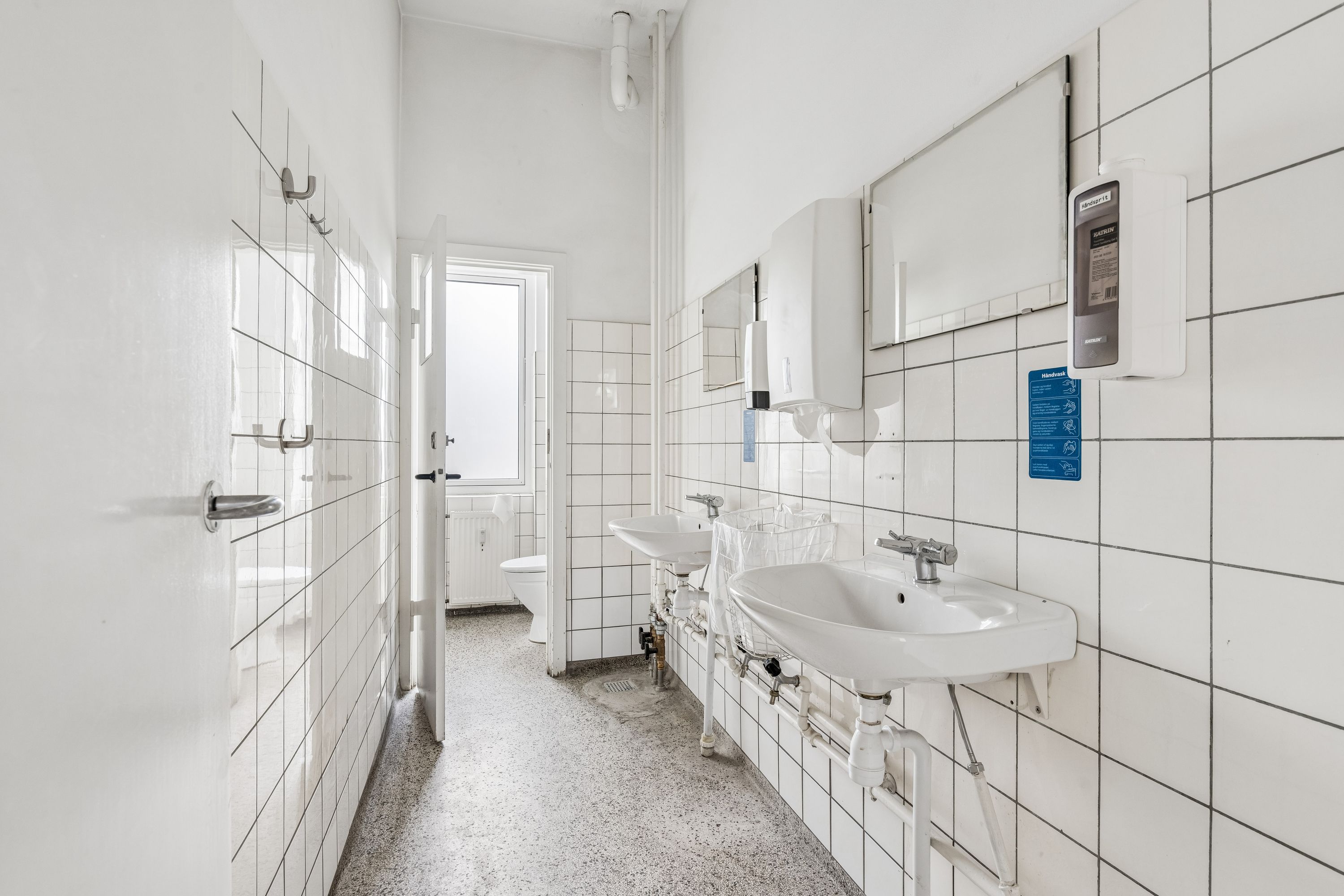 Ren toiletfacilitet med toilet, håndvask og hånddesinfektionsdispenser. Lokaler med hvide teglfliser og gulvbelægning i granit. Håndspriter og håndklæder er til rådighed.