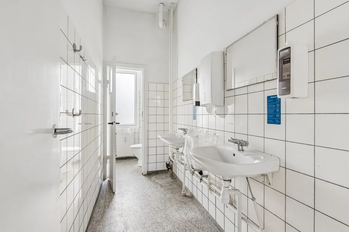 Ren toiletfacilitet med toilet, håndvask og hånddesinfektionsdispenser. Lokaler med hvide teglfliser og gulvbelægning i granit. Håndspriter og håndklæder er til rådighed.
