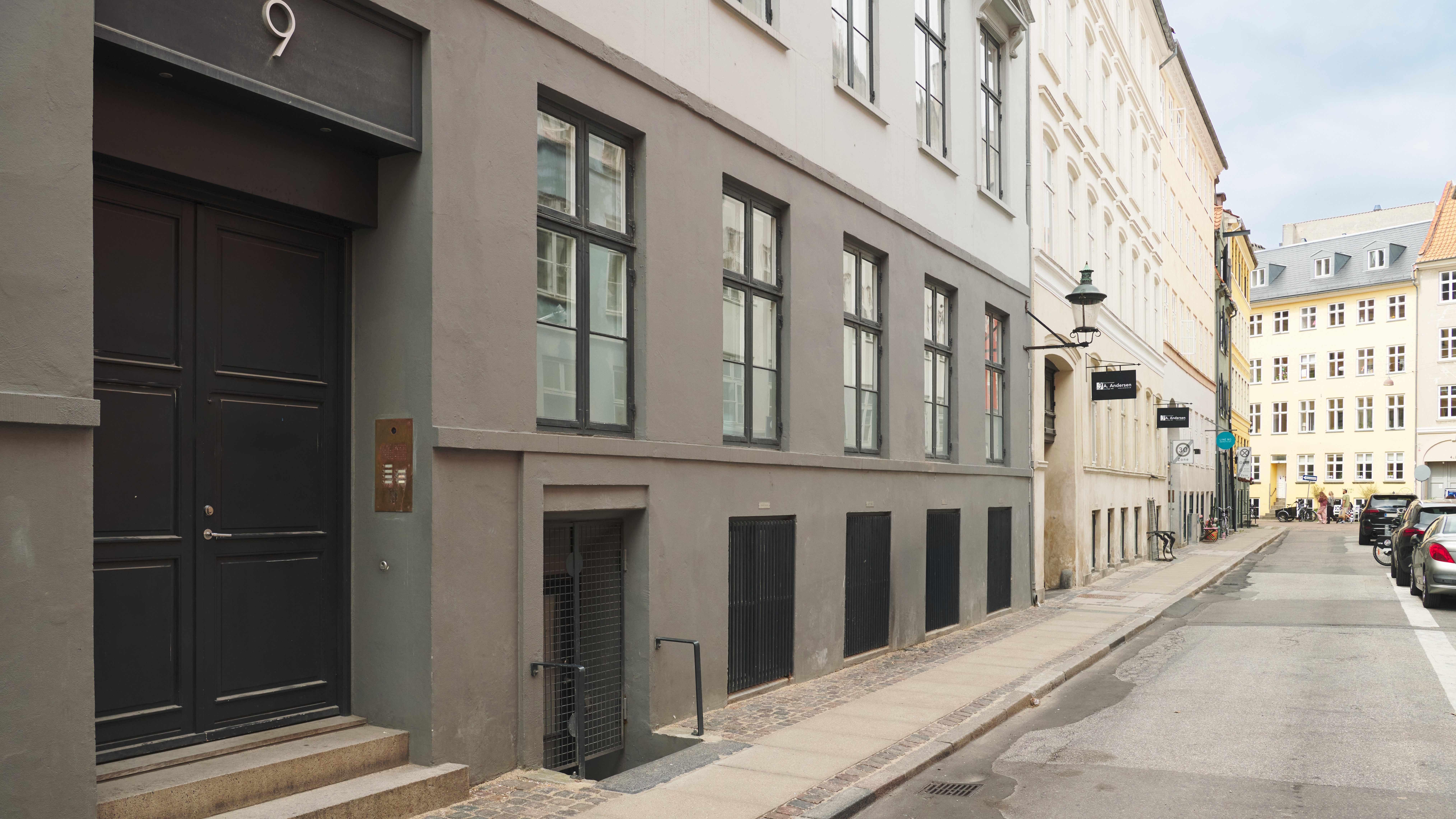 To store sorte døre til et erhvervslejemål med nummer 9. Mørke metaldøre med søjler og skrift. Vinduer med gardiner og lyse glasruder.