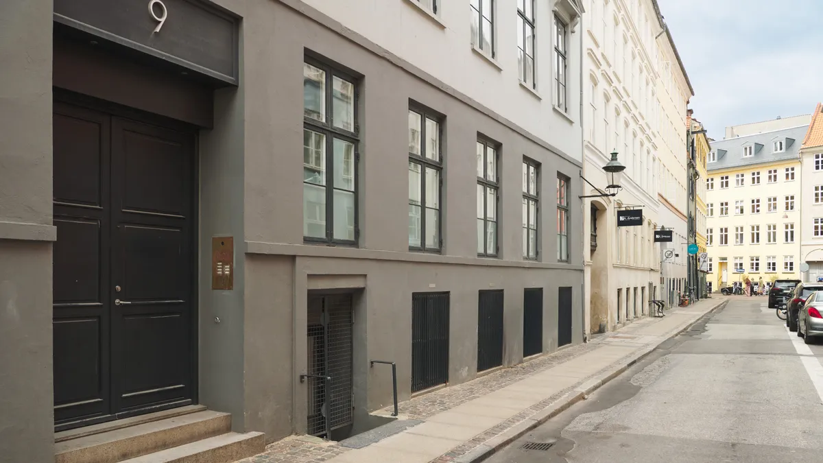To store sorte døre til et erhvervslejemål med nummer 9. Mørke metaldøre med søjler og skrift. Vinduer med gardiner og lyse glasruder.