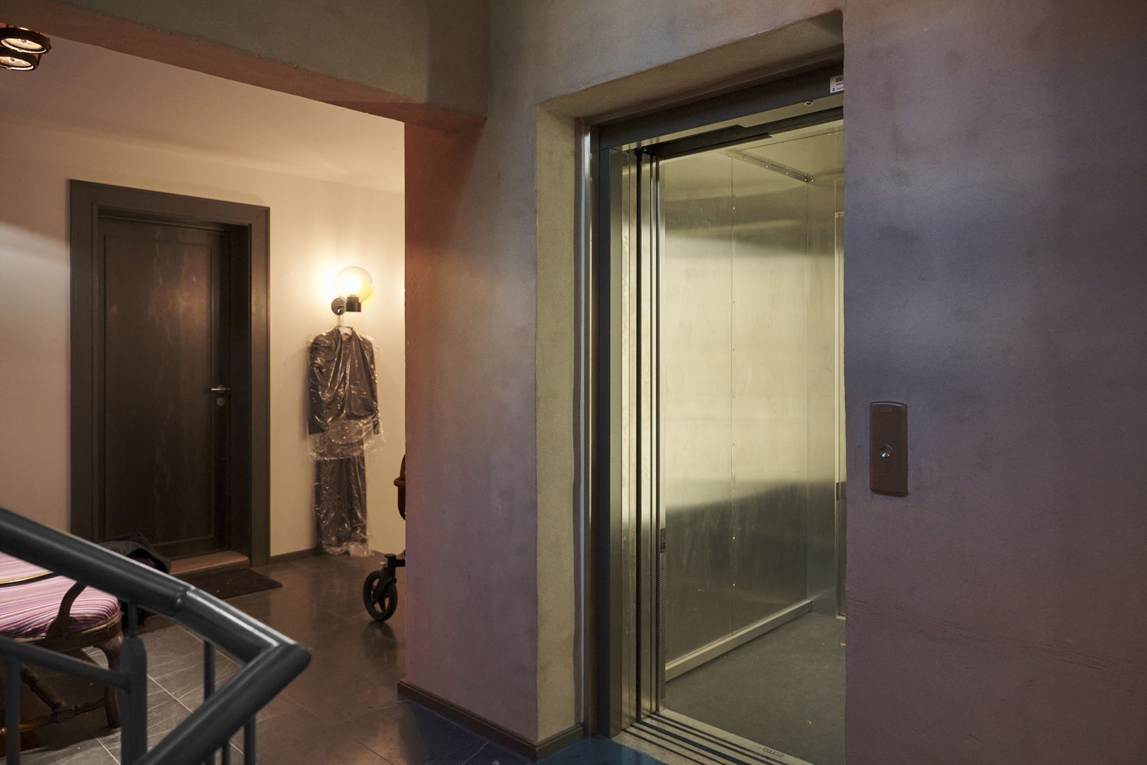 Her ses et glaskledet elevator med åben dør og gulv i gult marmor. Der er skråtag og lysekroner i loftet