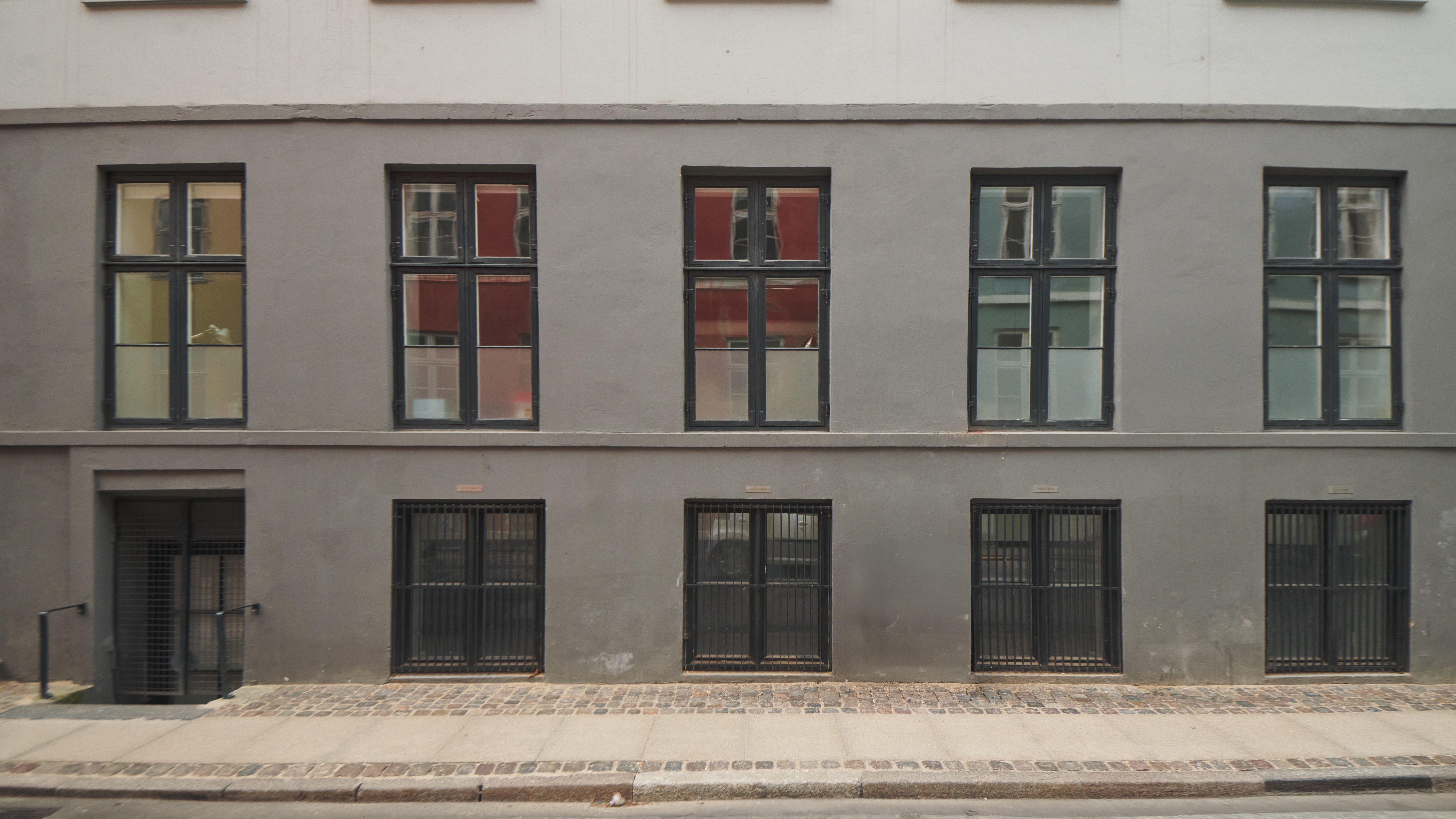 Opfindsomt renoveret bygning med lyse vinduerne og slanke søjler. Store, sortrammede ruder og lyseglasdøre. Brolægget fortov og slanke, sortmetals rækværk.