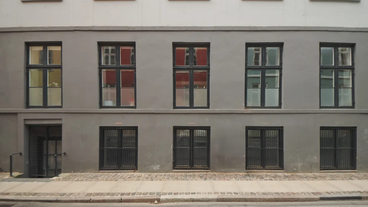 Opfindsomt renoveret bygning med lyse vinduerne og slanke søjler. Store, sortrammede ruder og lyseglasdøre. Brolægget fortov og slanke, sortmetals rækværk.
