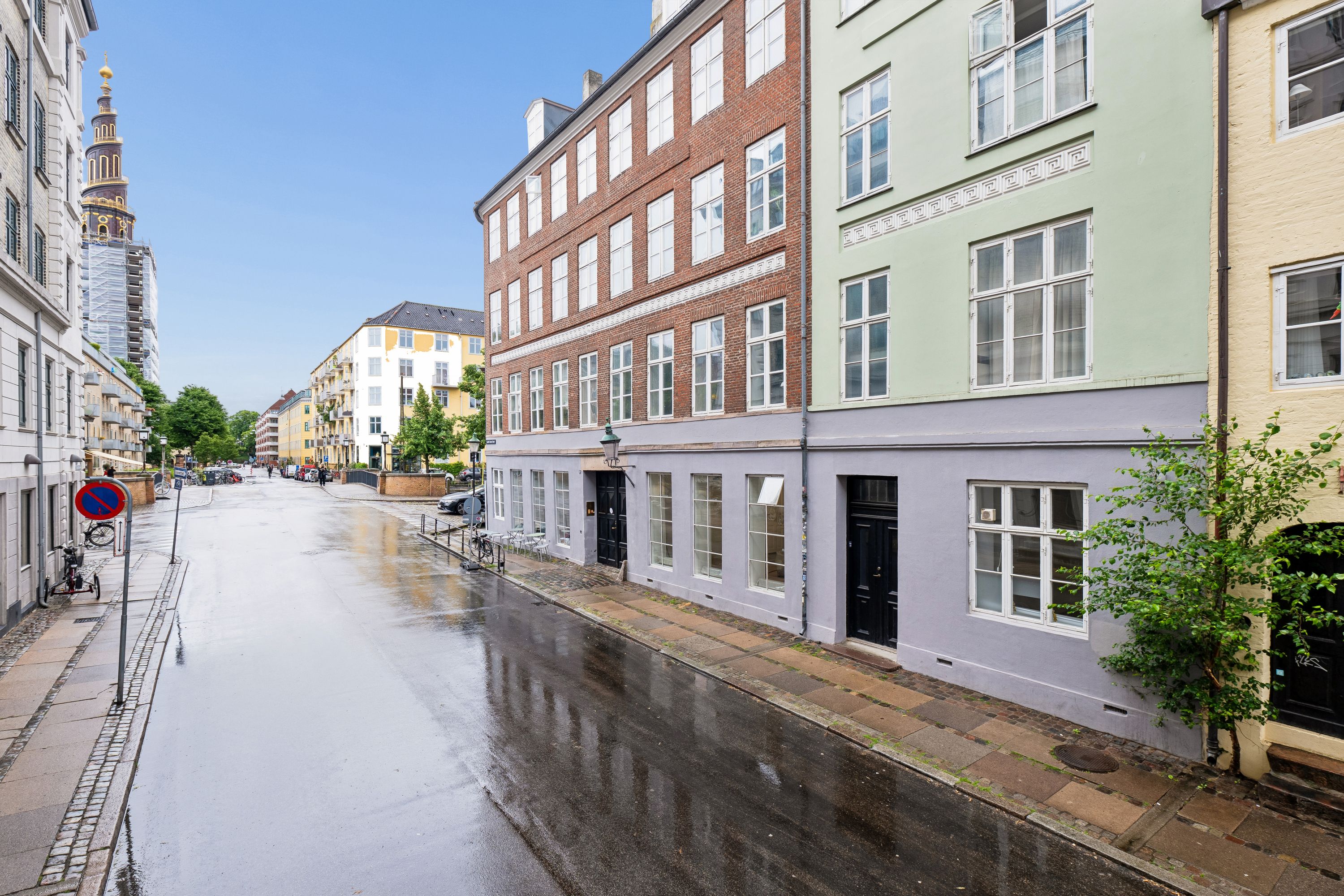 En vej i København med bygninger og parkerede biler, samt et skur og cykler langs kanten