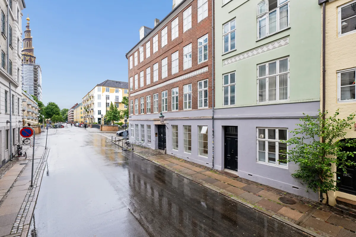 En vej i København med bygninger og parkerede biler, samt et skur og cykler langs kanten