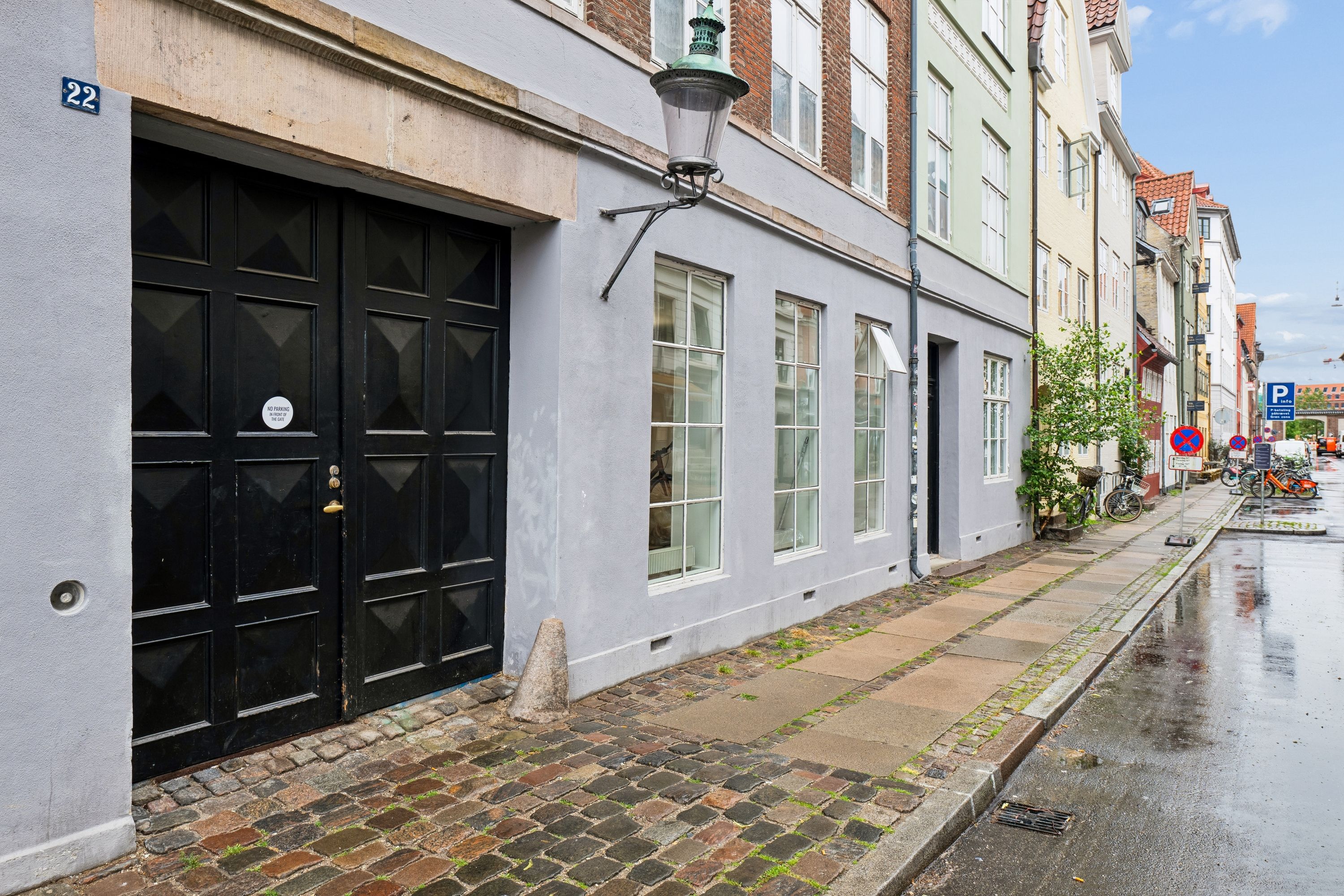 Københavnske bygning med røde mursten og mørke, store garageporte i nummer 22 på Sankt Annæ Gade, 1416 København K, med vej og cykler langs kanterne