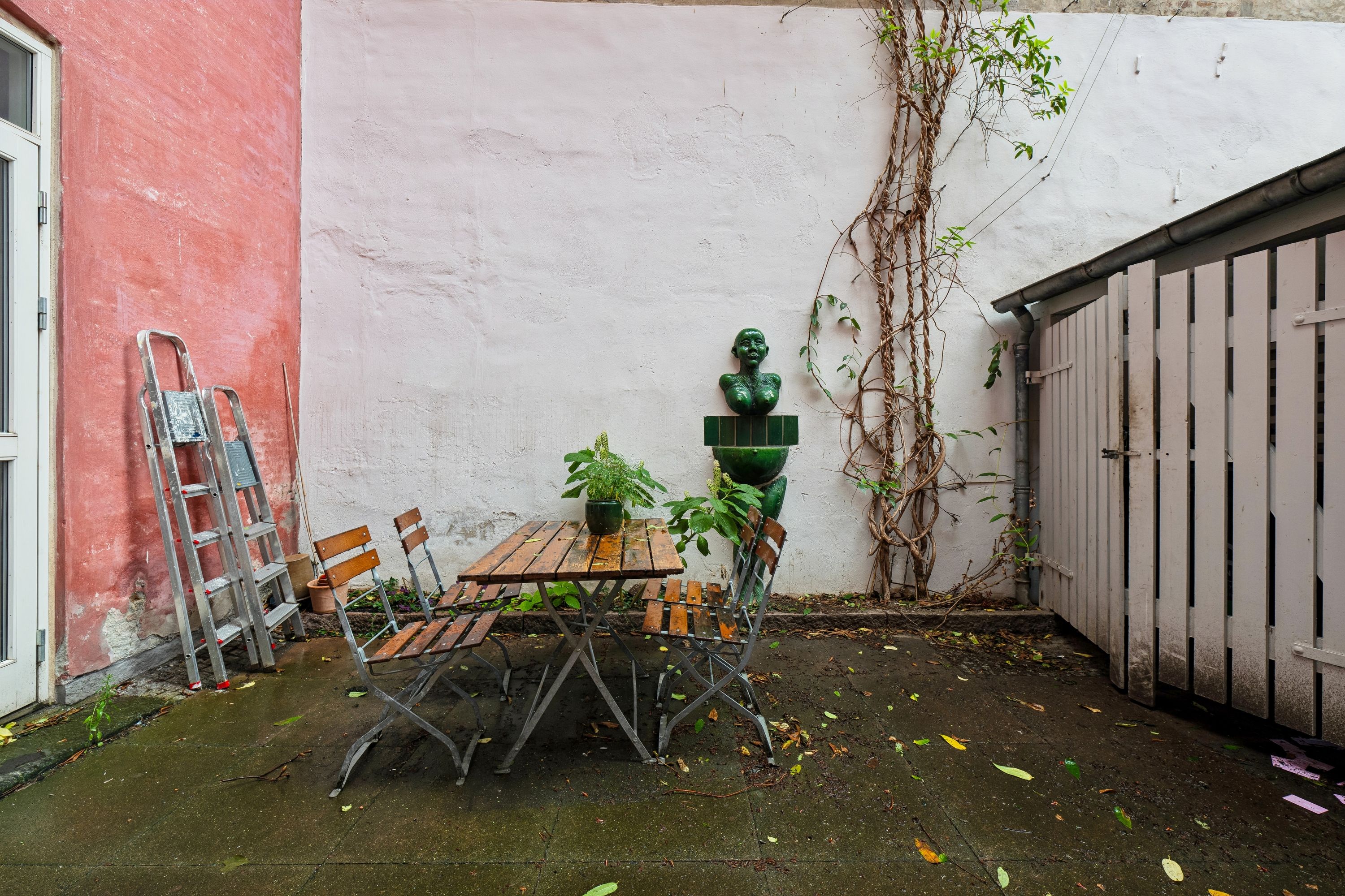 Kontor med terrasse og møbelsæt udendørs, busthus, skulptur og plante ved hvid mur i København