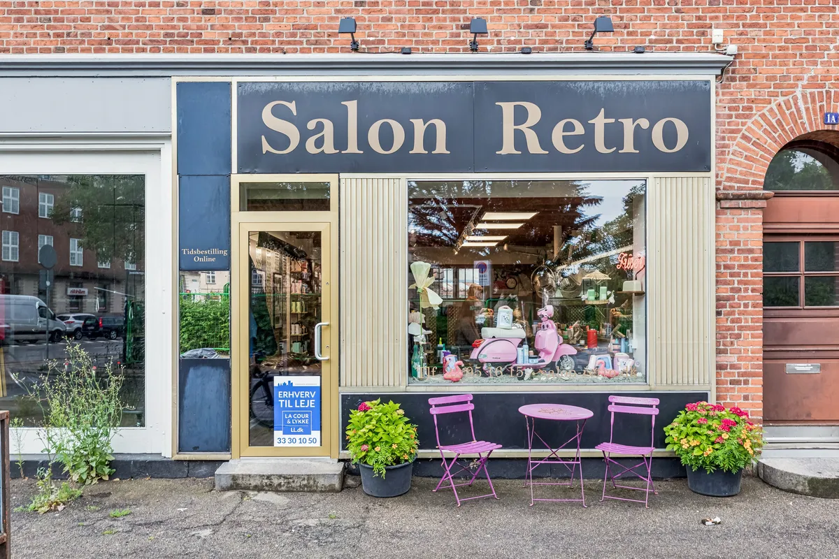 Lejlighedsvis butik til leje med terrassebord og stole og lyserøde planter og Salon Retro skilt på facaden.