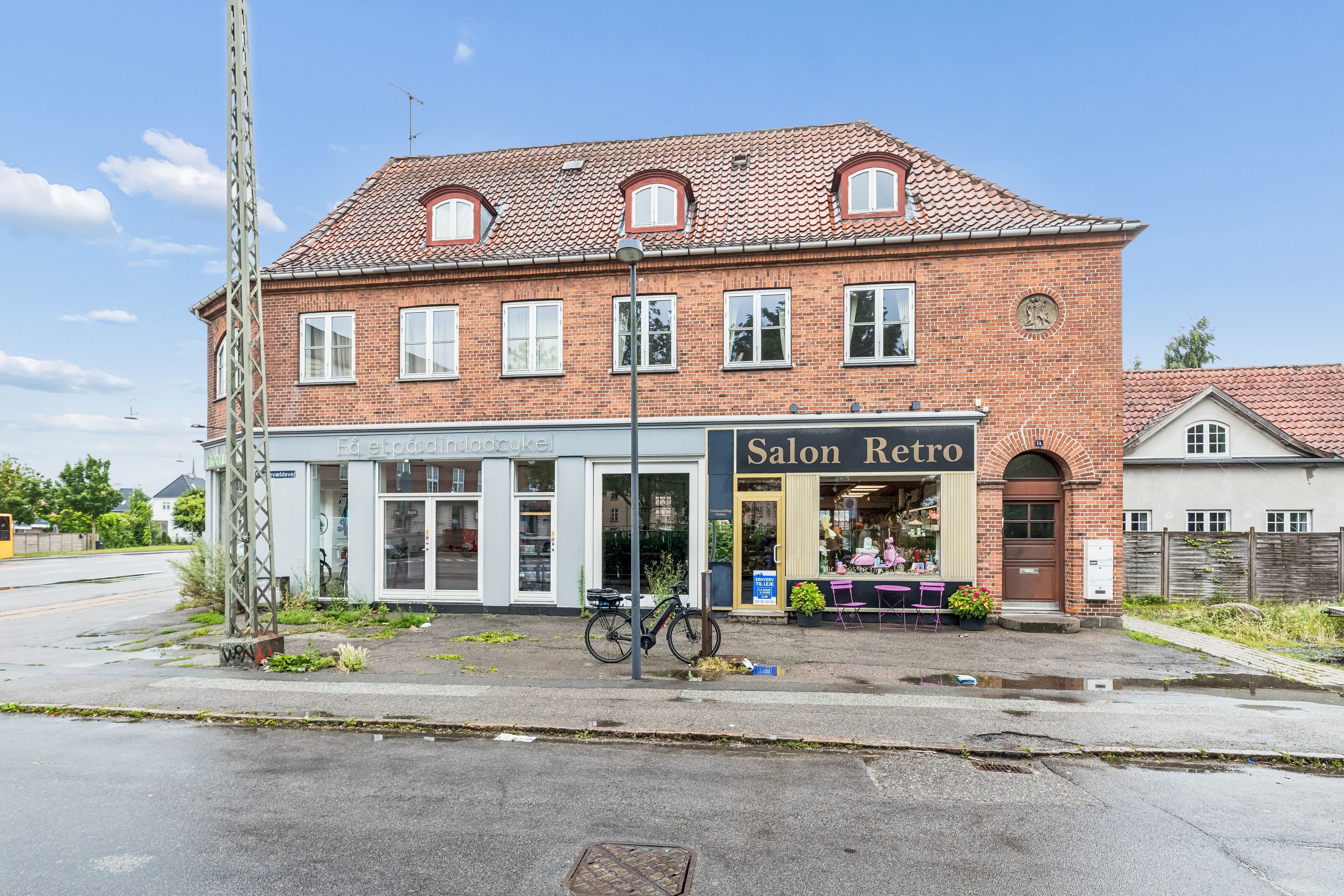 Salon Retro på Tryggevældevej 1A i Vanløse med lyse ruder og røde tag. Bicyle parkeret foran butikken, og planter og stole foran indgangen.