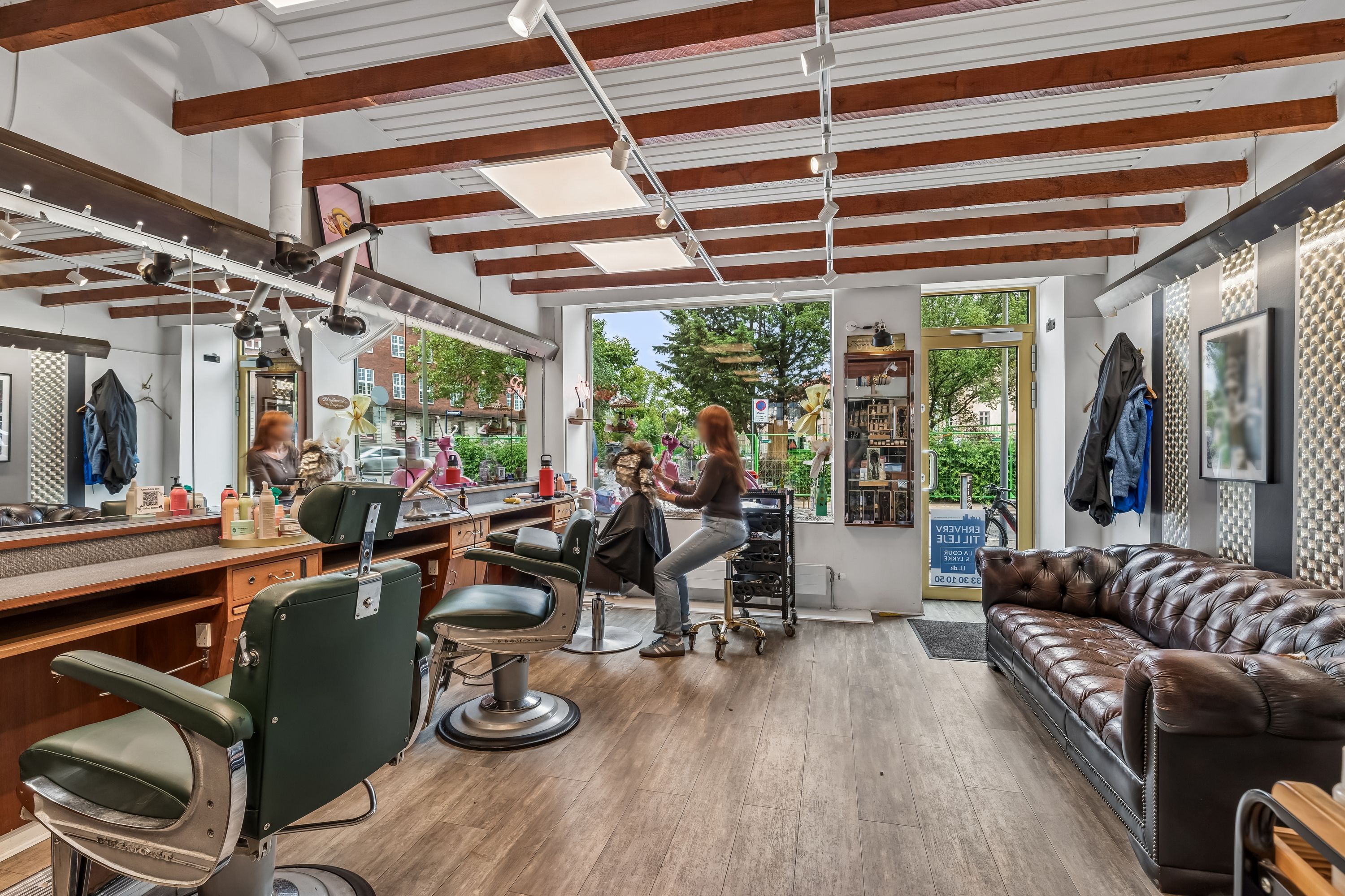 Et frisørsalon med træloft og lysegulv, barberstole og sæder, og en brun sofa til kunderne