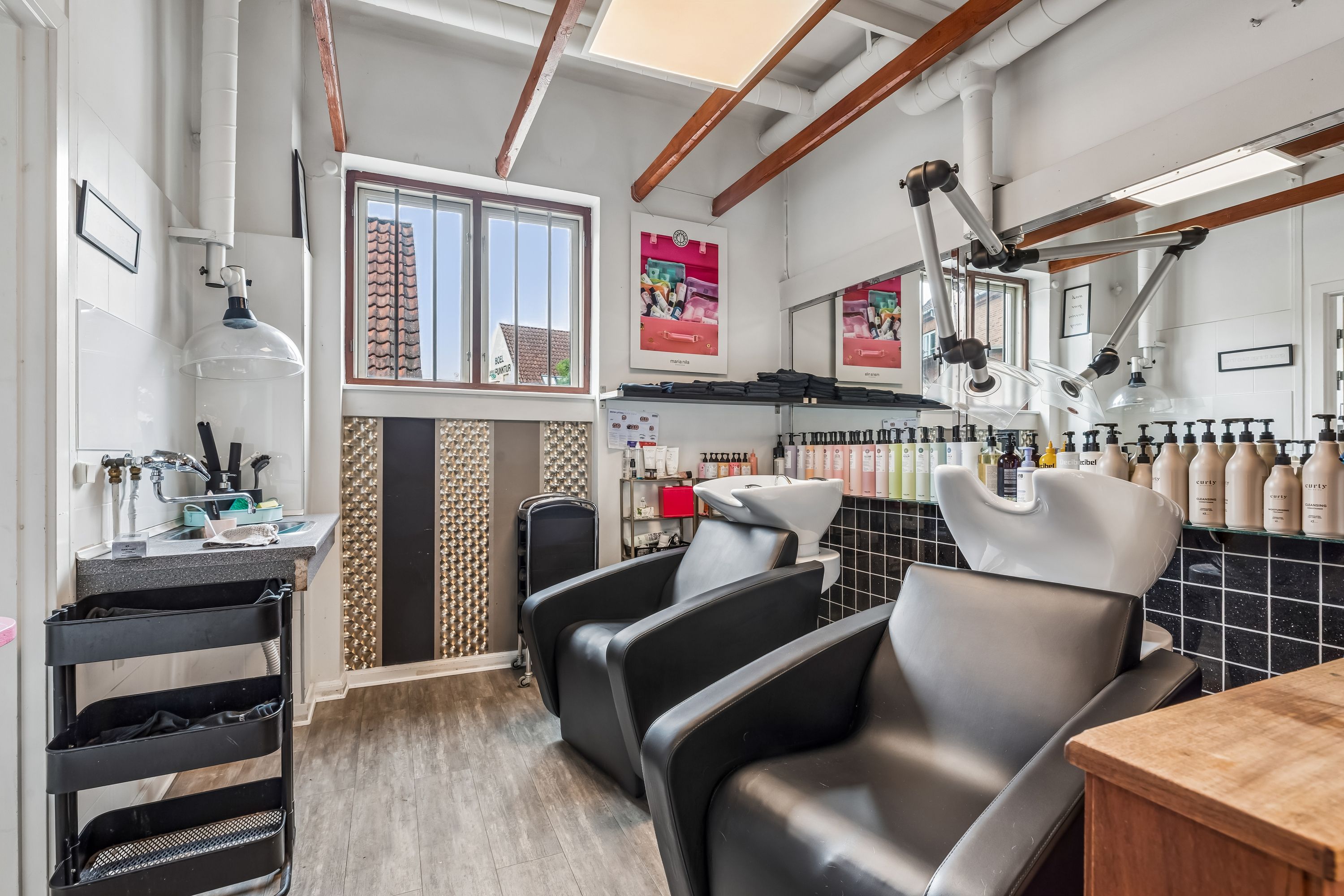 Salon med lyse farver og moderne interiør med to højryggede lænestol, skraldkurv, lyse gulvbelægning, spejl, vinduesglas og lyse skyggekast på væggen