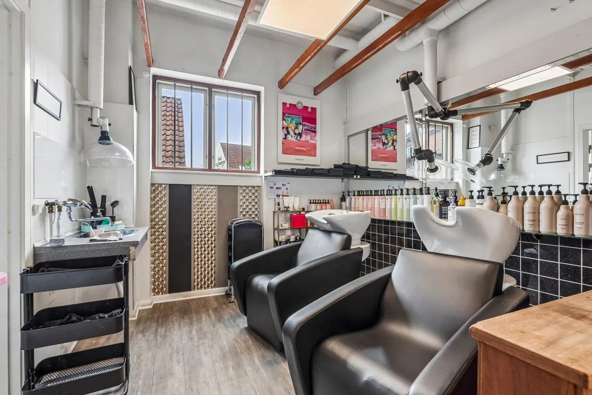 Salon med lyse farver og moderne interiør med to højryggede lænestol, skraldkurv, lyse gulvbelægning, spejl, vinduesglas og lyse skyggekast på væggen