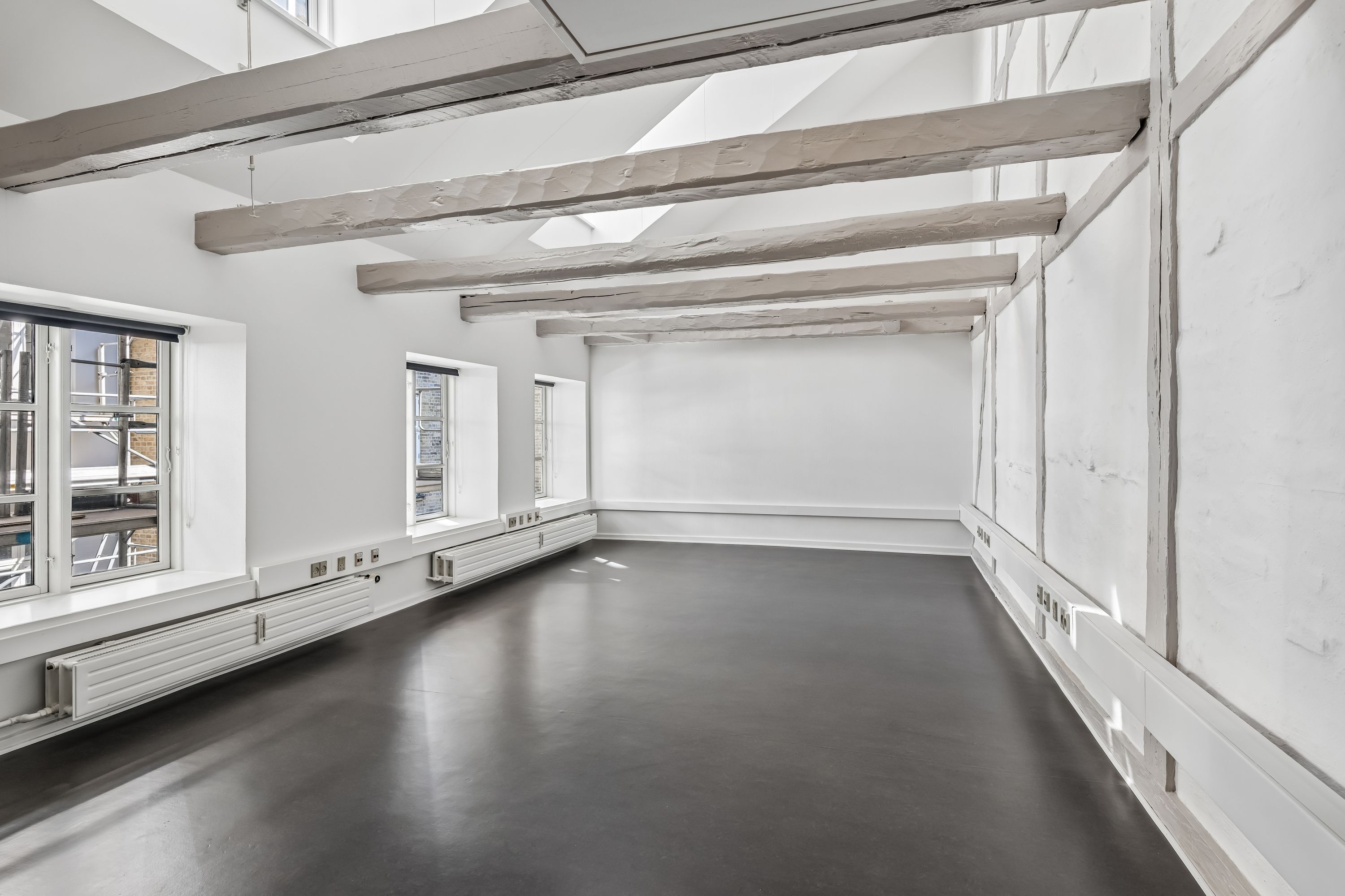 Lyst kontor med højloft og store vinduer mod gaden i København K. Vægge er hvide og gulve er mørke.